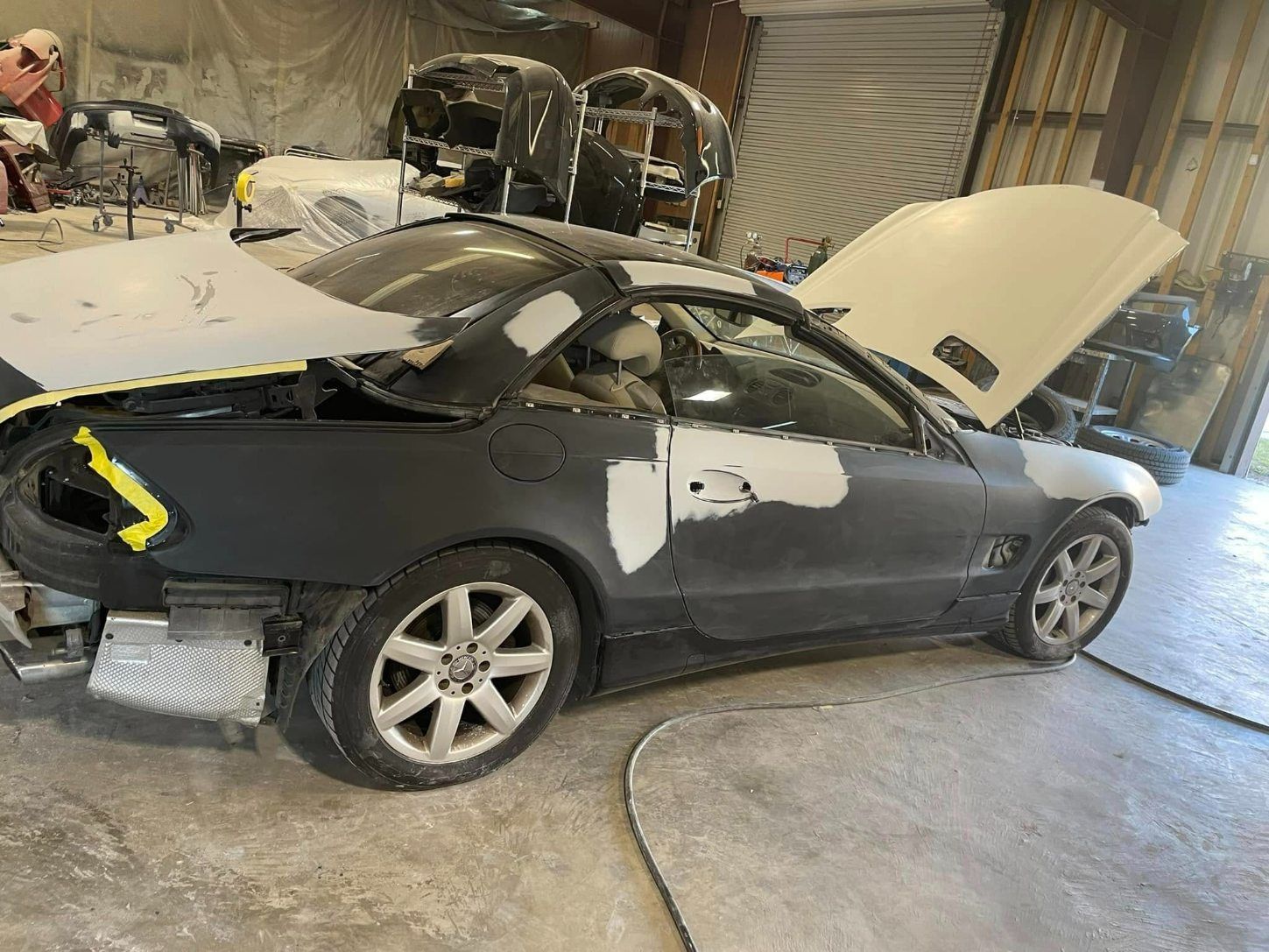 A car with its hood and trunk open, undergoing bodywork and primer in a workshop.