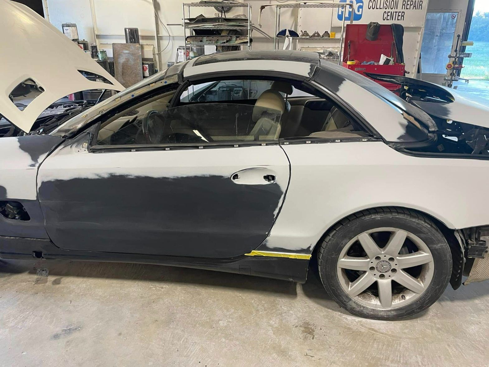 A side view of a white Mercedes-Benz SLK convertible undergoing body work in a garage, featuring a dark grey door panel.