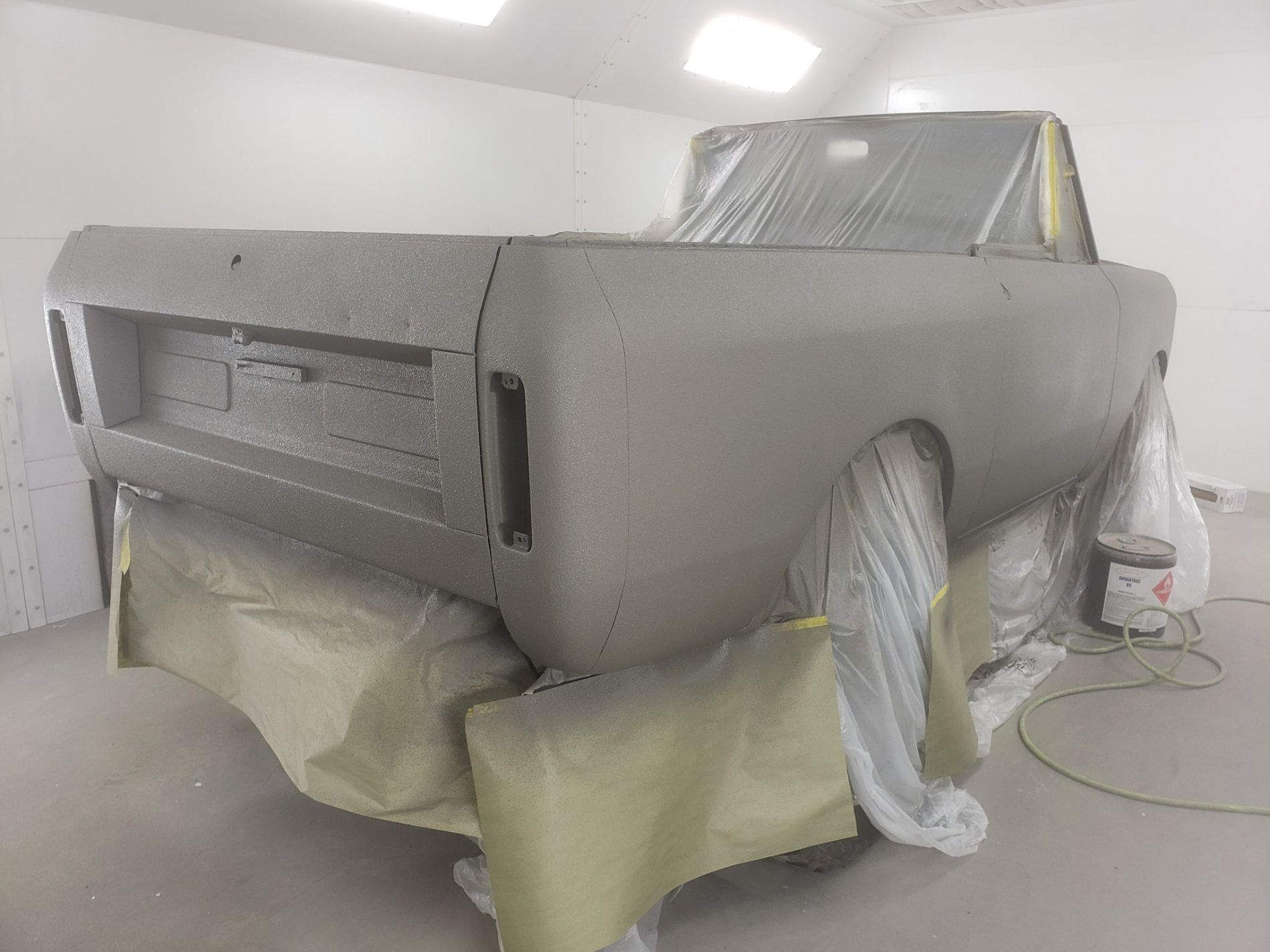 A grey, textured truck body in a masked-off spray booth, prepared for painting.