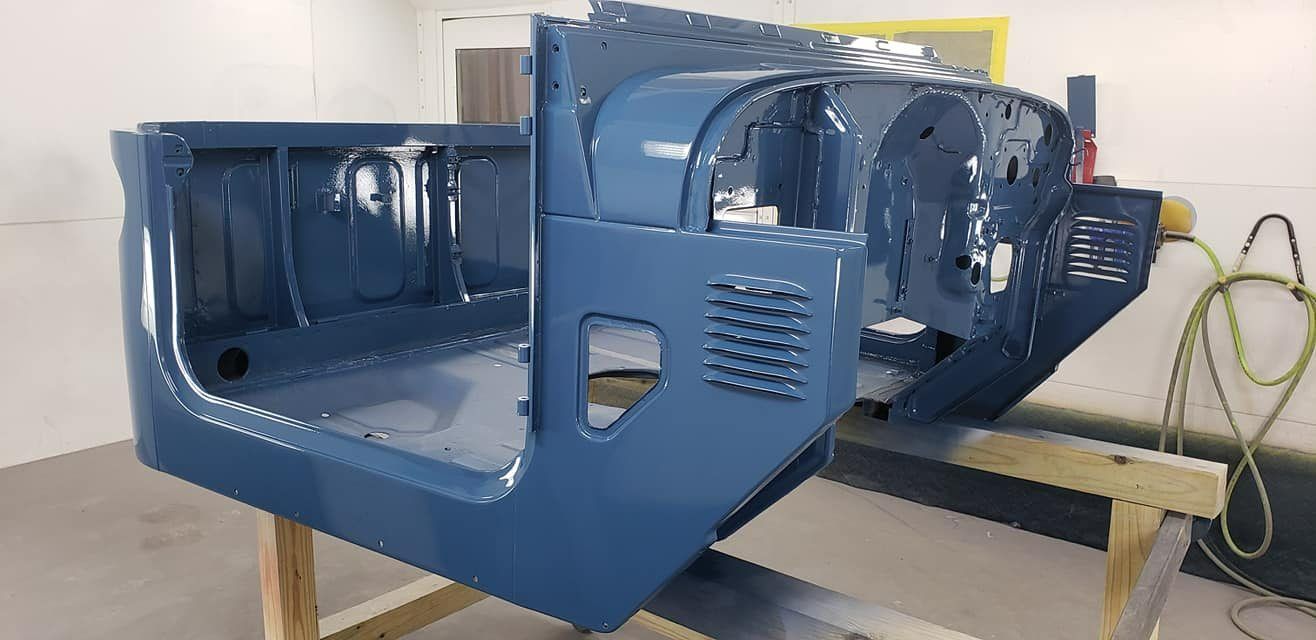 A blue Jeep tub body shell rests on a wooden frame inside a garage or workshop for painting or restoration.