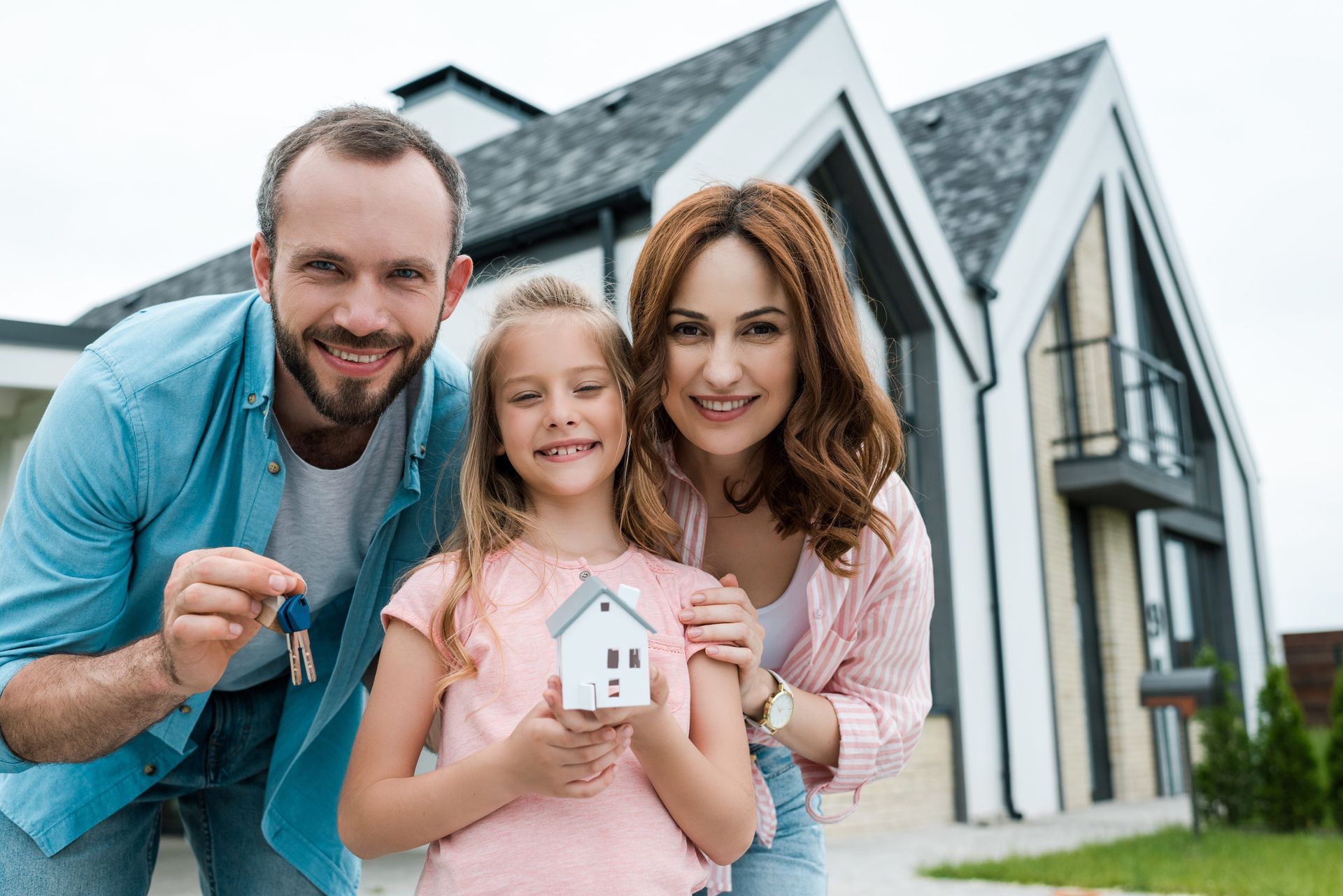 Smiling family holding a small house model in front of a modern home