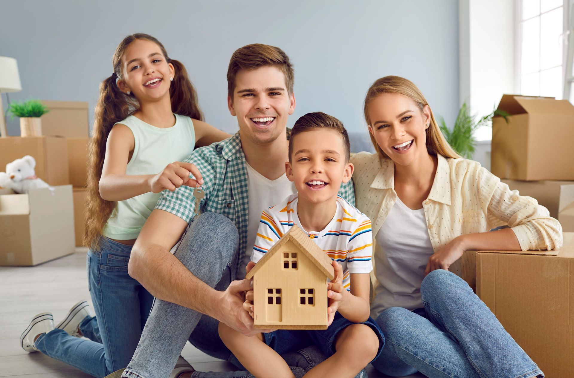Smiling family holding a wooden house model in a bright living room with moving boxes
