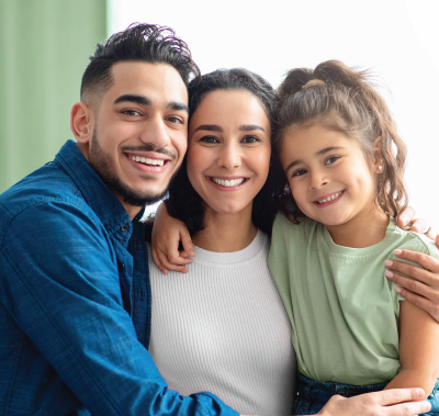 Three smiling people sitting close together on a couch, wearing blue, white, and green tops.