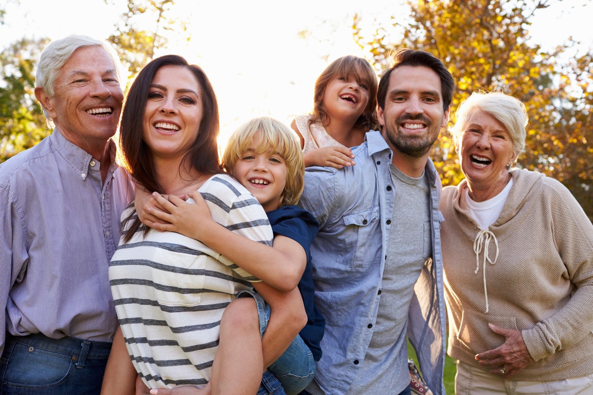 Smiling family group outdoors in autumn, standing close together in warm sunlight.