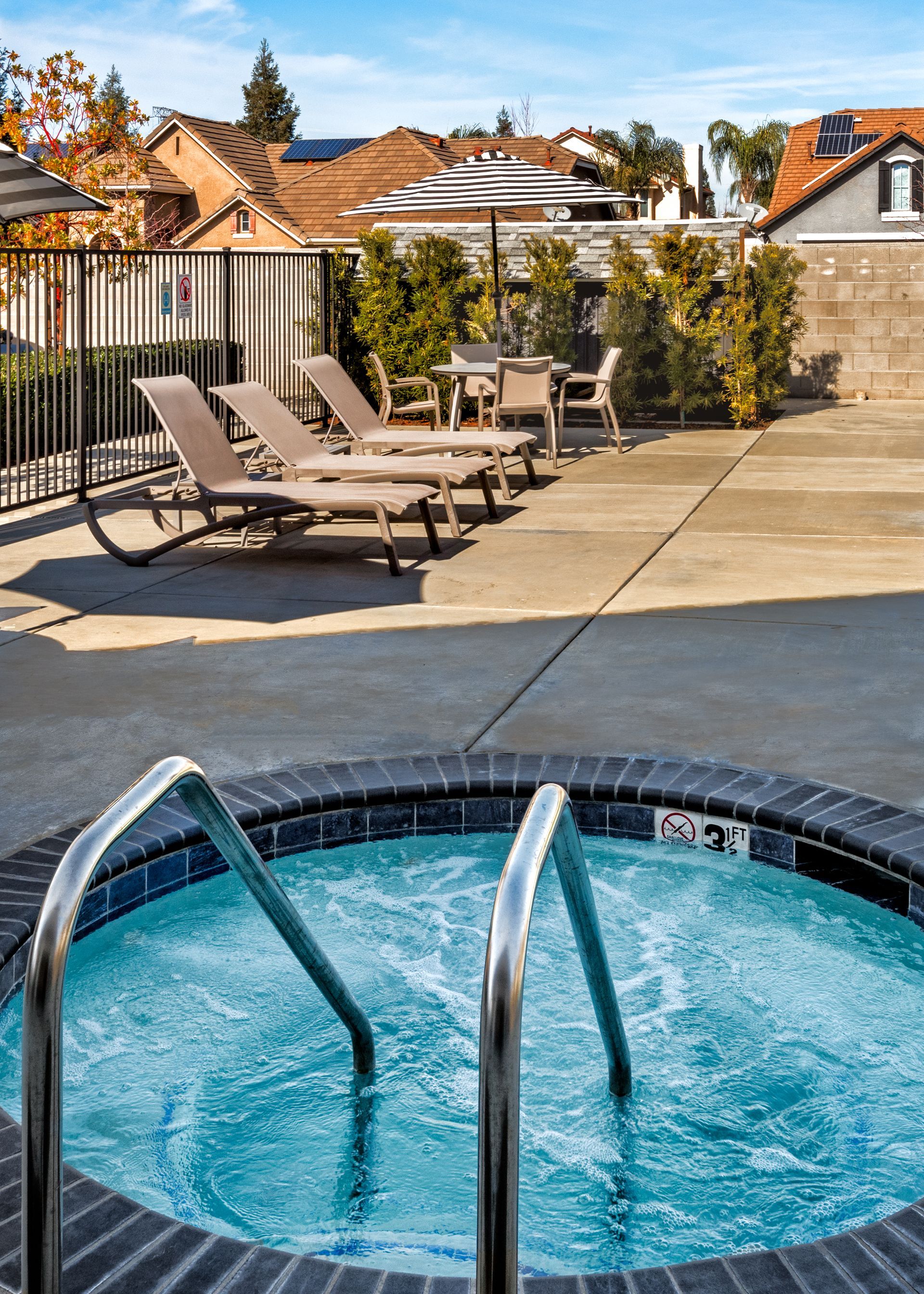 Hot tub with a view of lounge chairs and buildings under a bright blue sky.