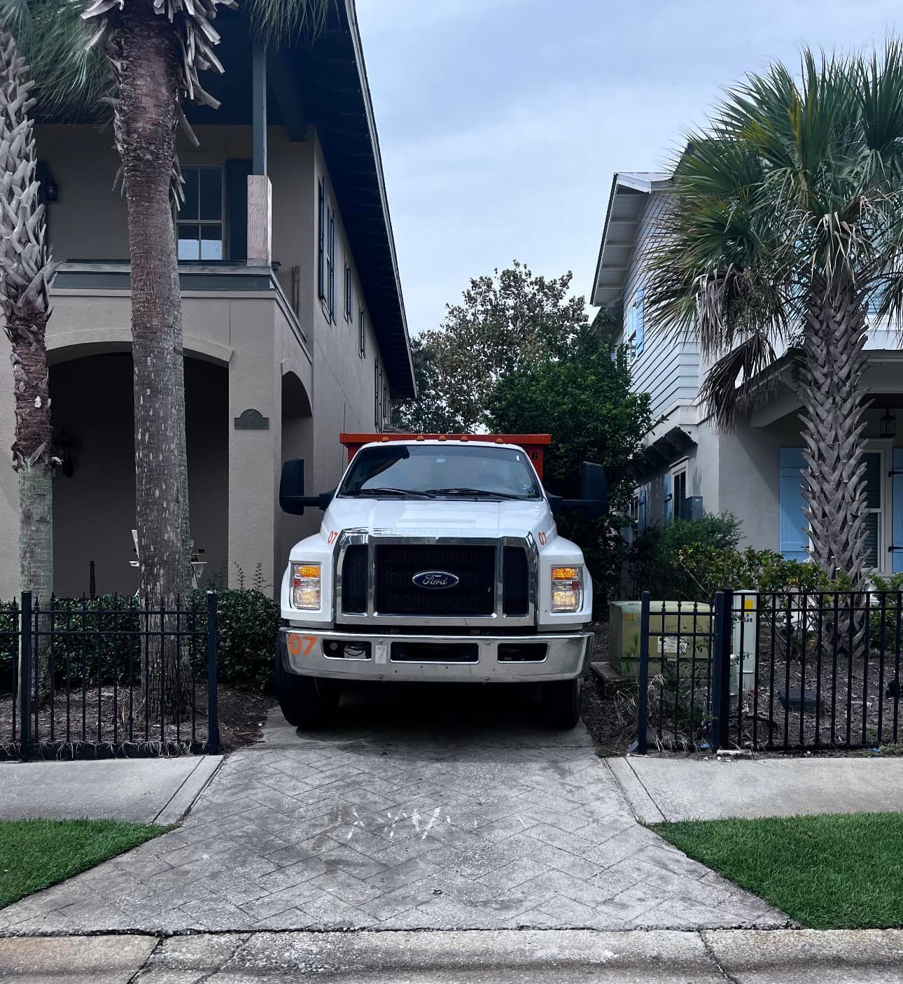 White Ford truck parked in a driveway between two houses, with palm trees and a black fence. White Ford truck parked in a driveway between two houses, with palm trees and a black fence.