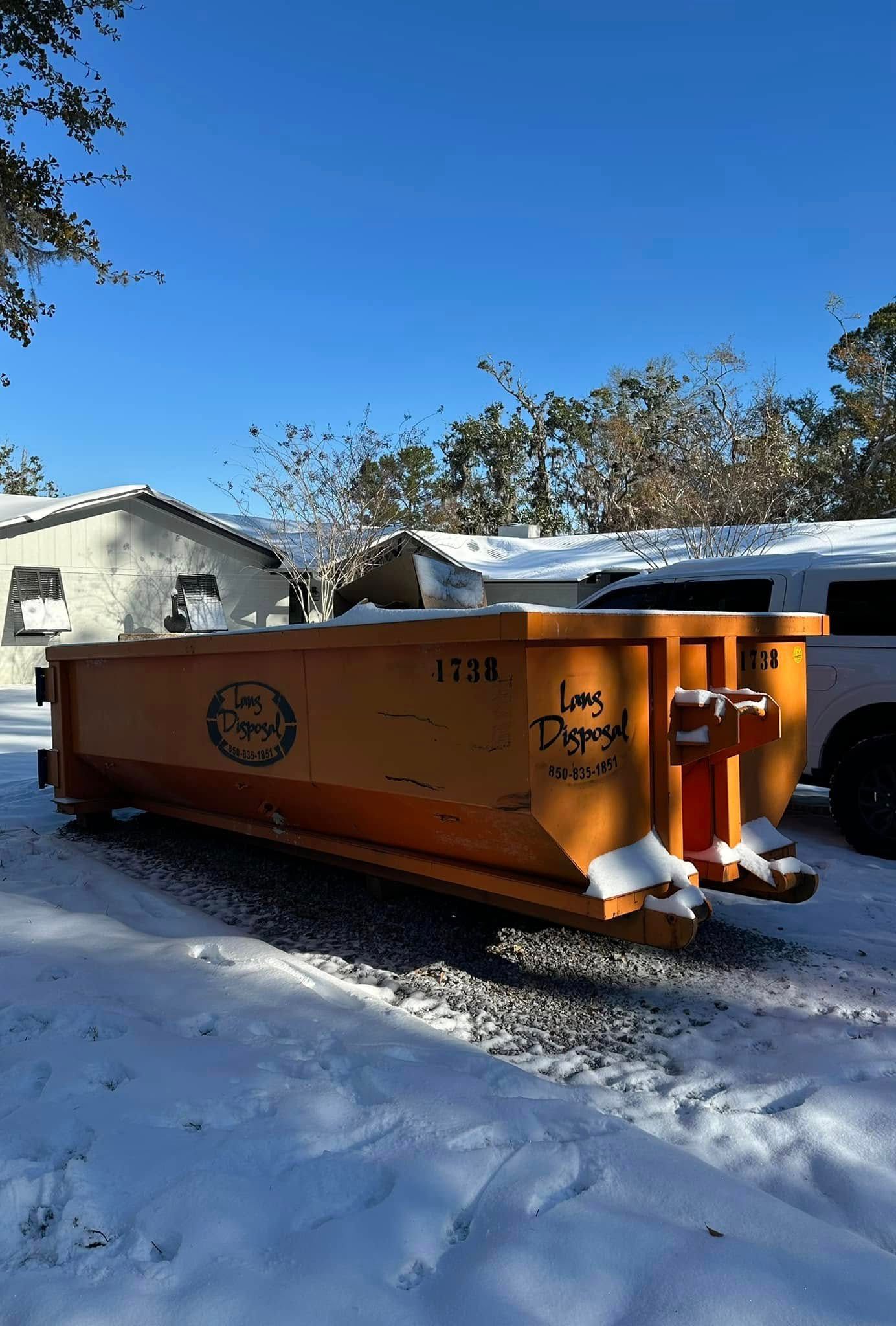 Orange dumpster in a snowy yard beside a house under a clear blue sky. Orange dumpster in a snowy yard beside a house under a clear blue sky.