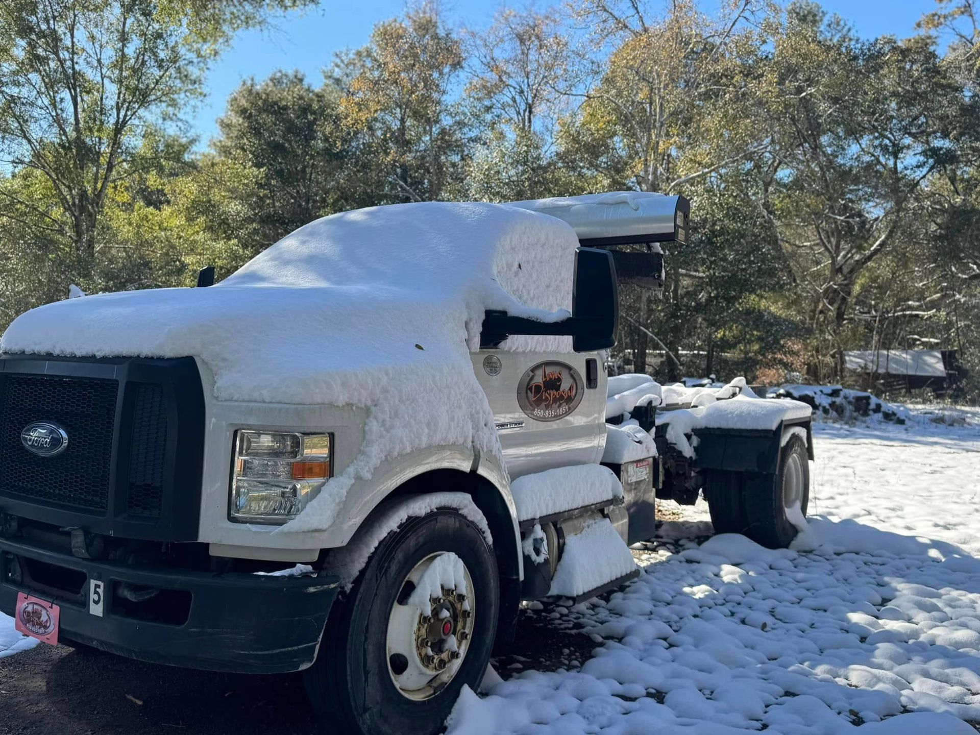 Snow-covered white semi-truck parked outdoors in a snowy wooded area