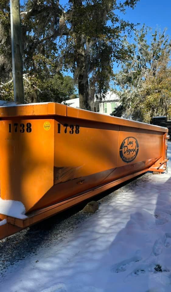 Orange construction dumpster on snowy ground beside trees, marked with the number 1738. Orange construction dumpster on snowy ground beside trees, marked with the number 1738.