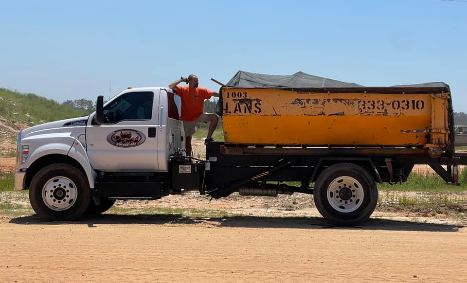 White utility truck with orange cargo bed parked on a dirt road in a rural area under a blue sky