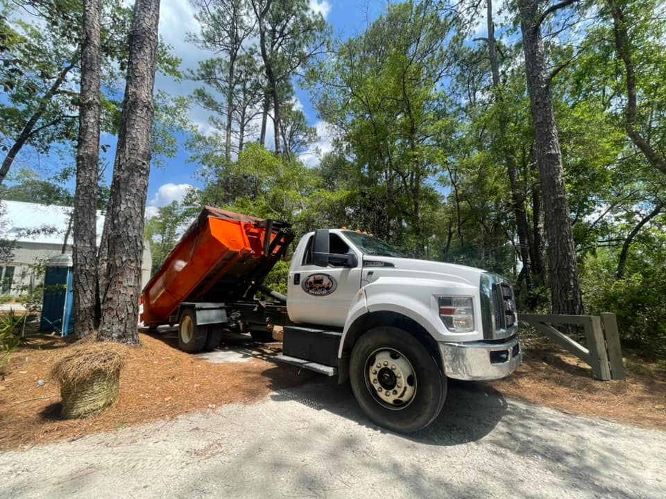 White dump truck with raised orange bed on a dirt driveway among pine trees and rocks White dump truck with raised orange bed on a dirt driveway among pine trees and rocks
