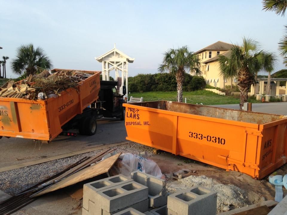 Orange dumpsters at a construction site with rubble and concrete blocks in the foreground