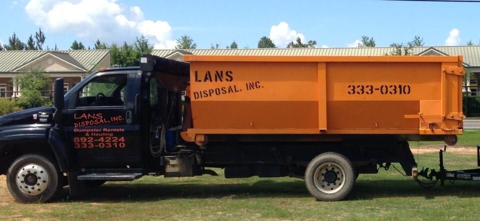 Orange dump truck parked on grass, labeled “Lans Disposal, Inc.”
