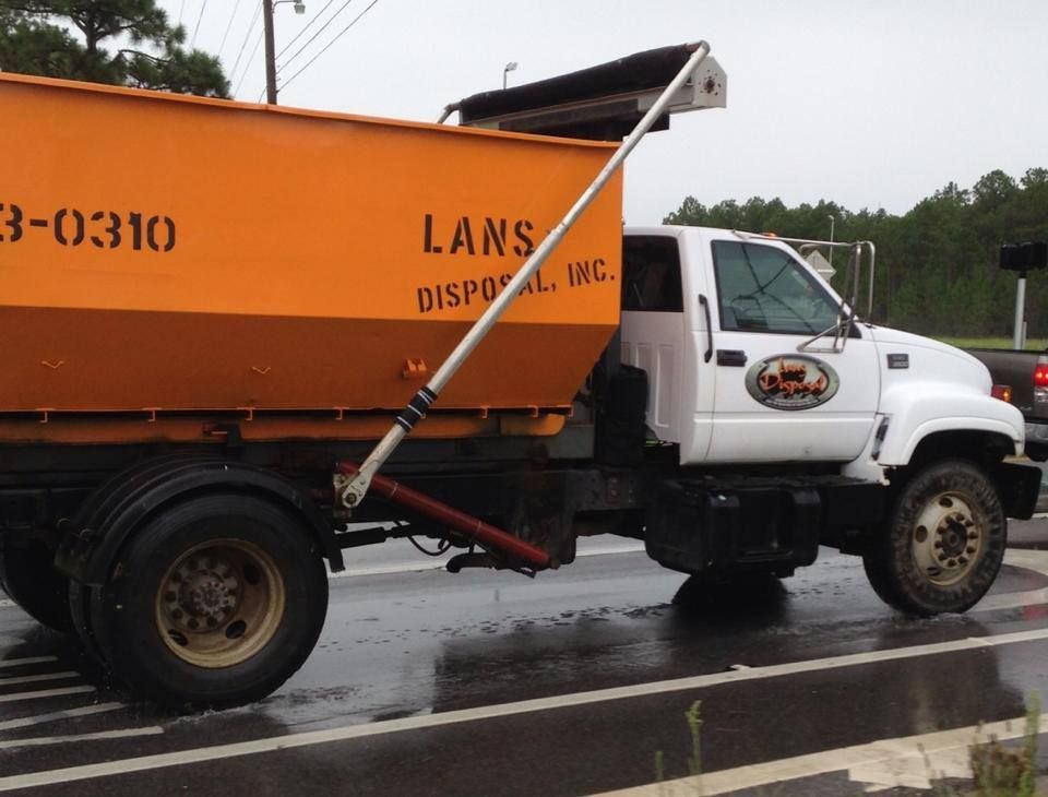 Orange-and-white garbage truck driving on a wet road in a rainy setting