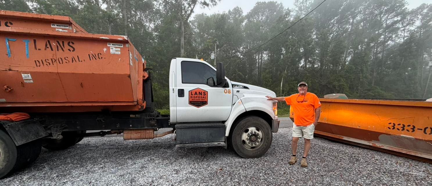 White tow truck and orange dump truck on a foggy roadside, with a worker in orange standing beside them.