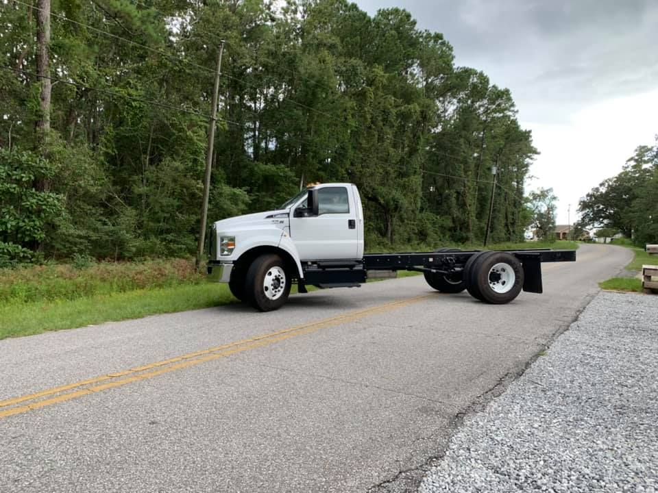 White cab truck chassis parked on a rural road beside trees and gravel shoulder