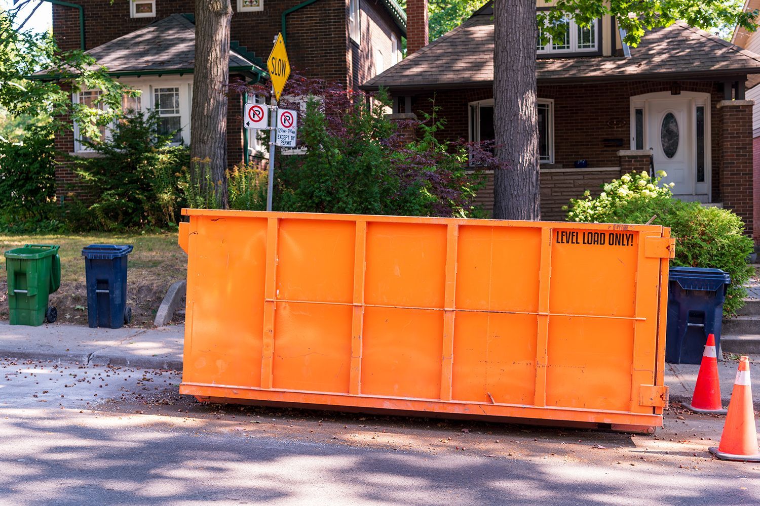 Orange construction dumpster on a street with trash bins and traffic cones in a residential neighborhood Orange construction dumpster on a street with trash bins and traffic cones in a residential neighborhood