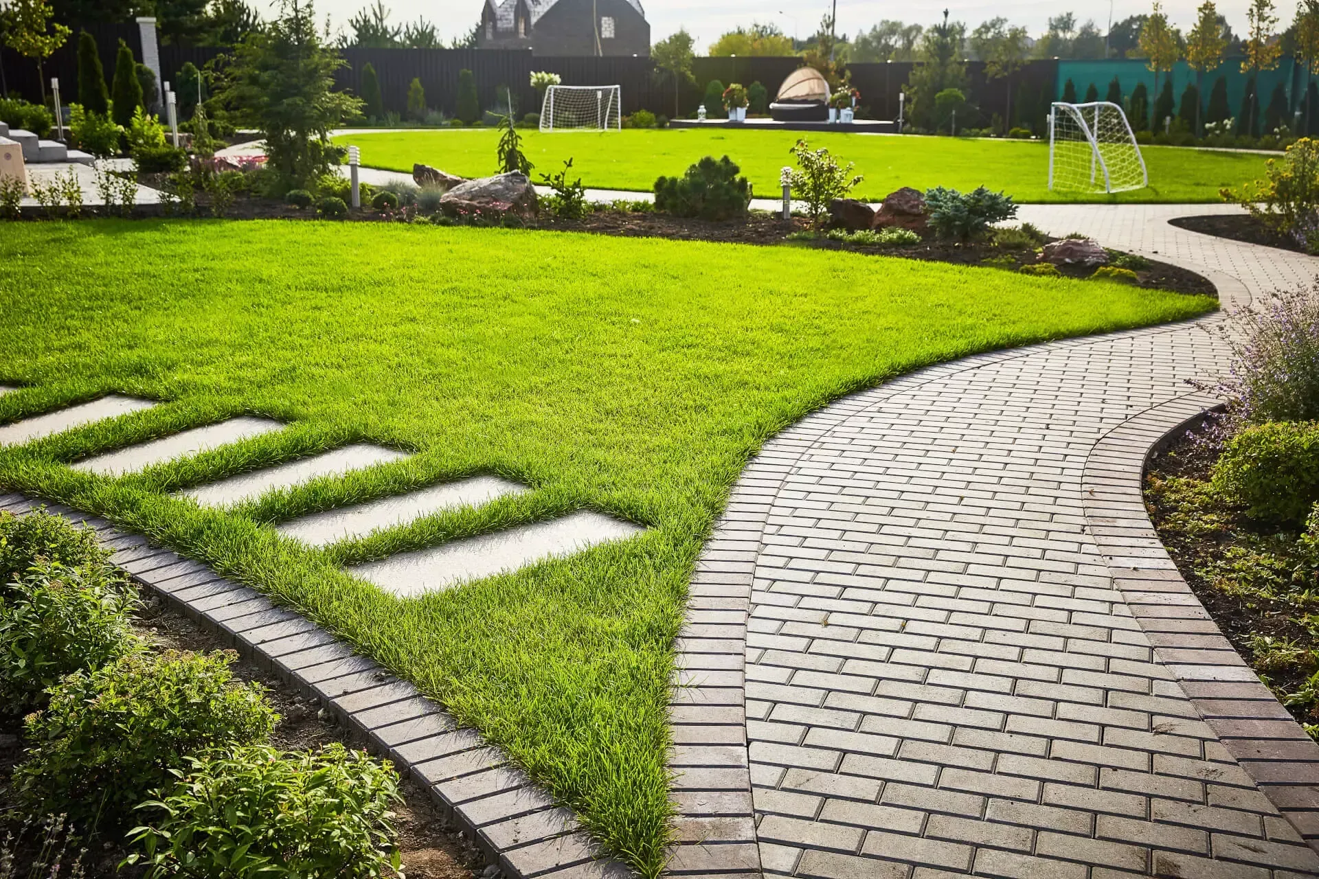 A brick walkway leading to a lush green field in a garden.