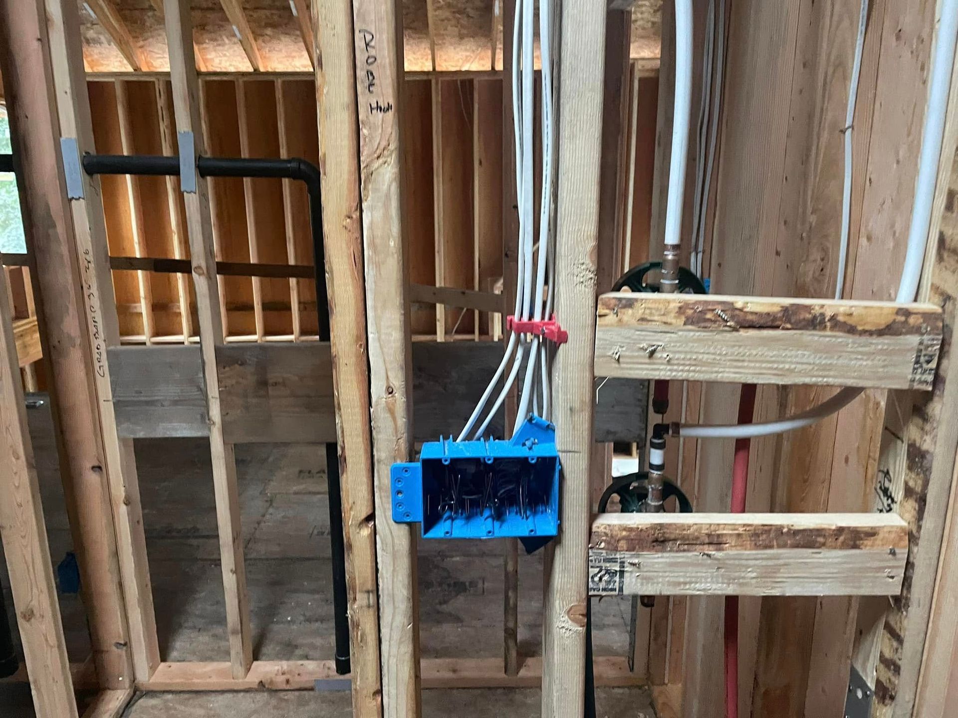 Blue electrical box with wires mounted on unfinished wooden wall framing