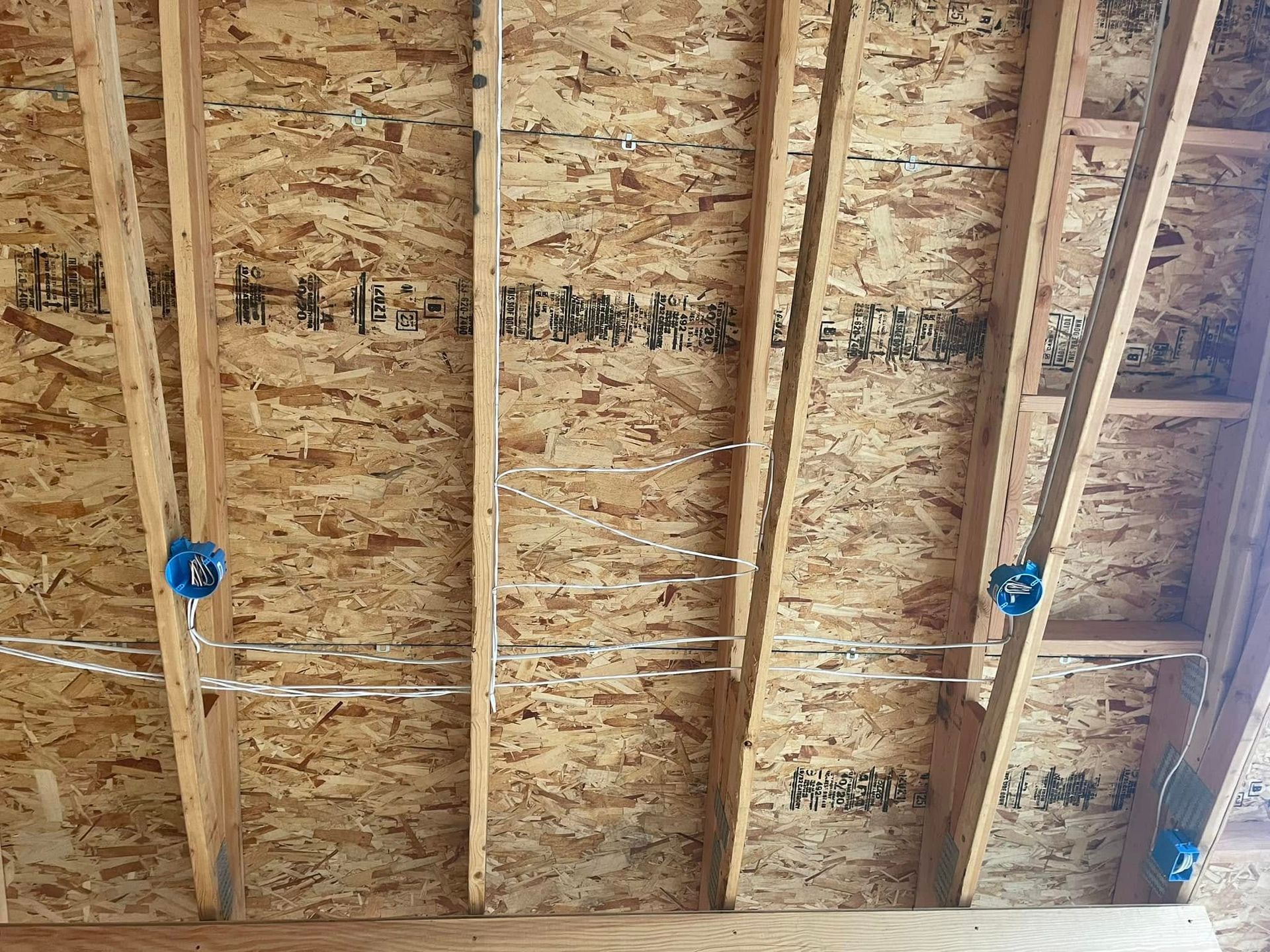 Unfinished plywood ceiling with exposed wooden rafters and blue electrical boxes.