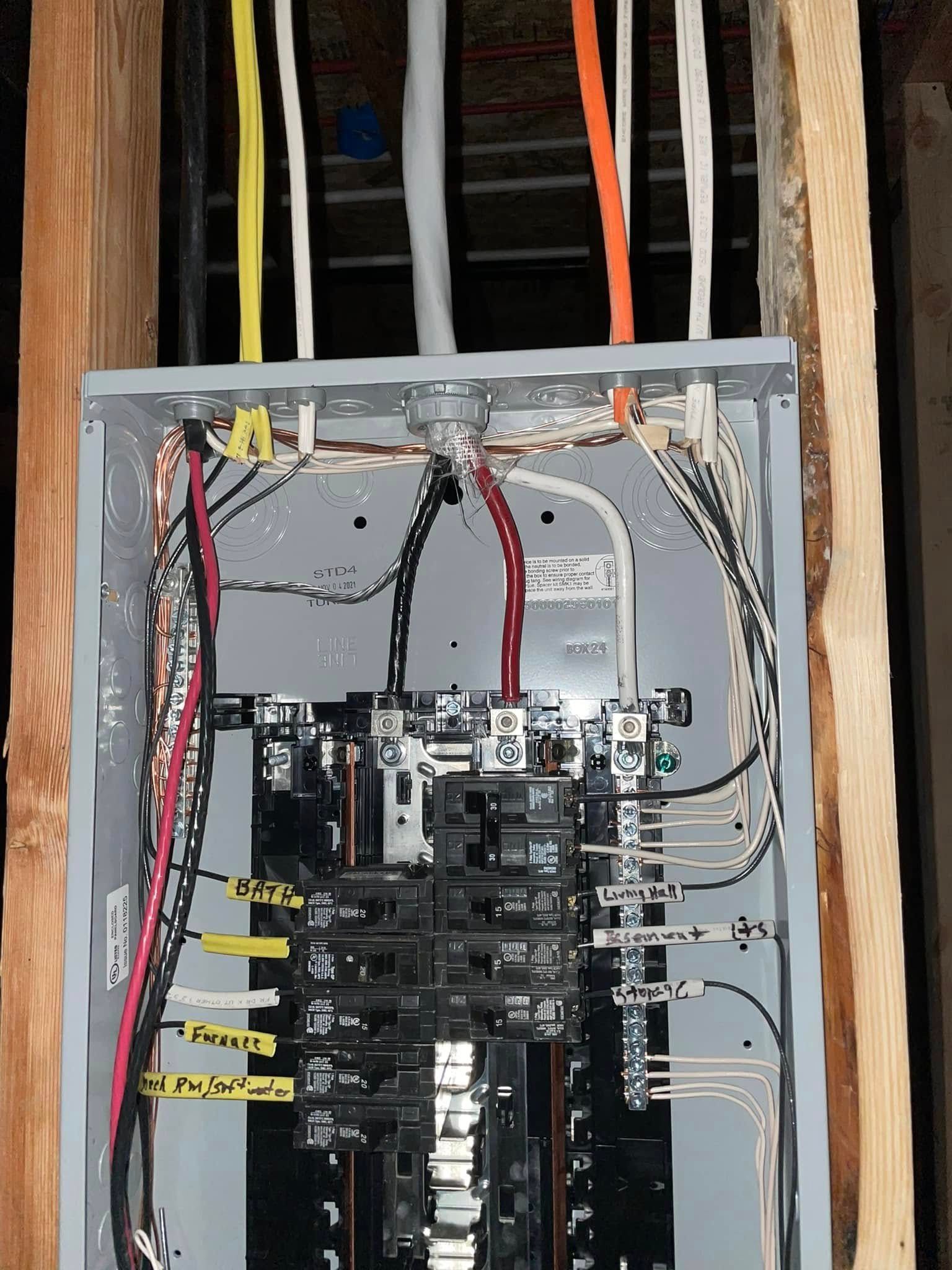 Open electrical breaker panel with wiring and labeled circuits inside a wall cavity