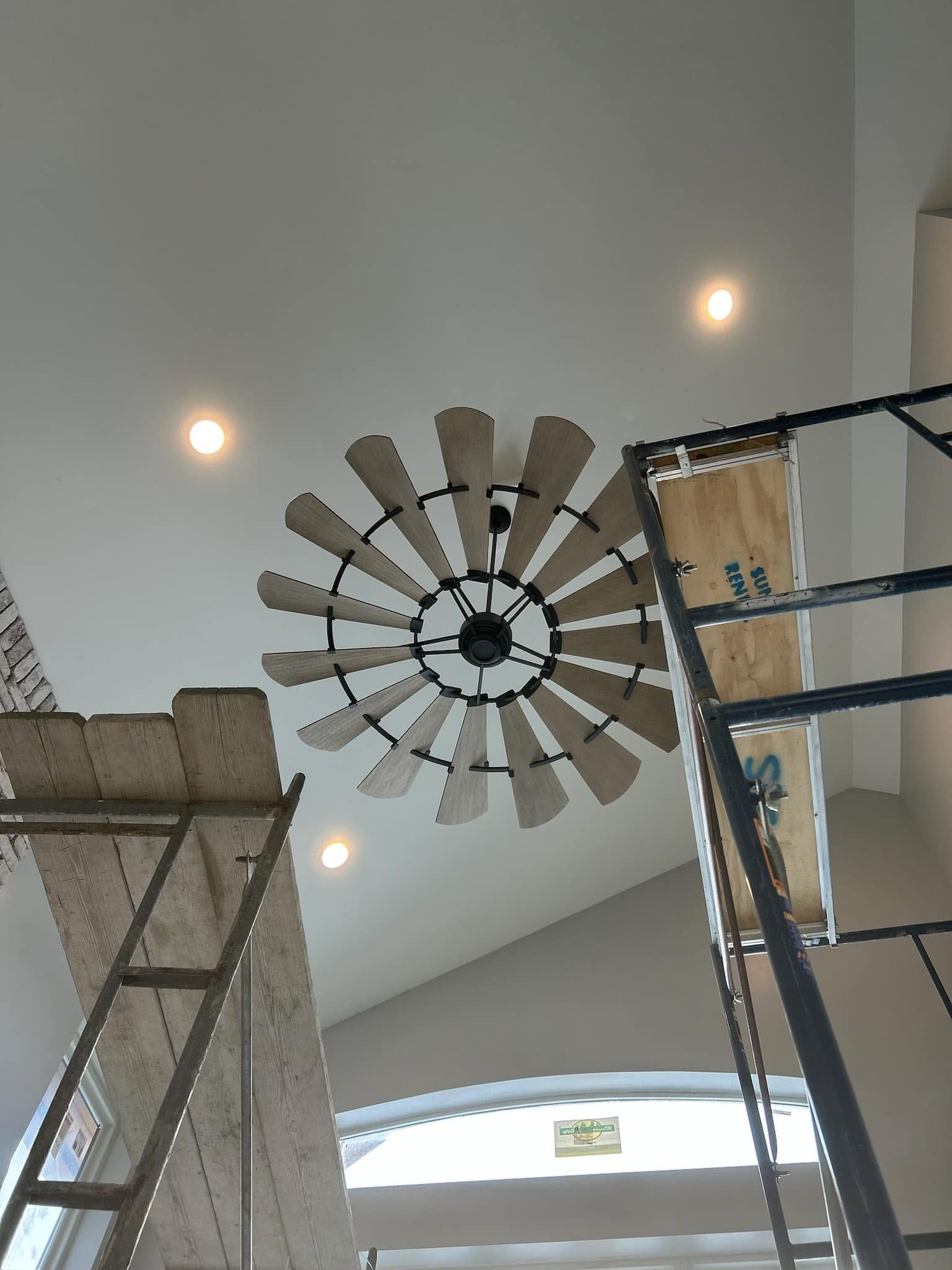 Ceiling with a large fan-shaped light fixture and recessed lights, viewed between two ladders or scaffolds.