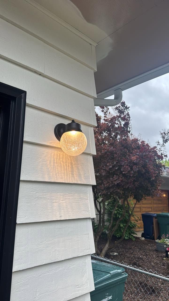 Heart-shaped wall sconce on white siding beside a porch, with a backyard and cloudy sky beyond.