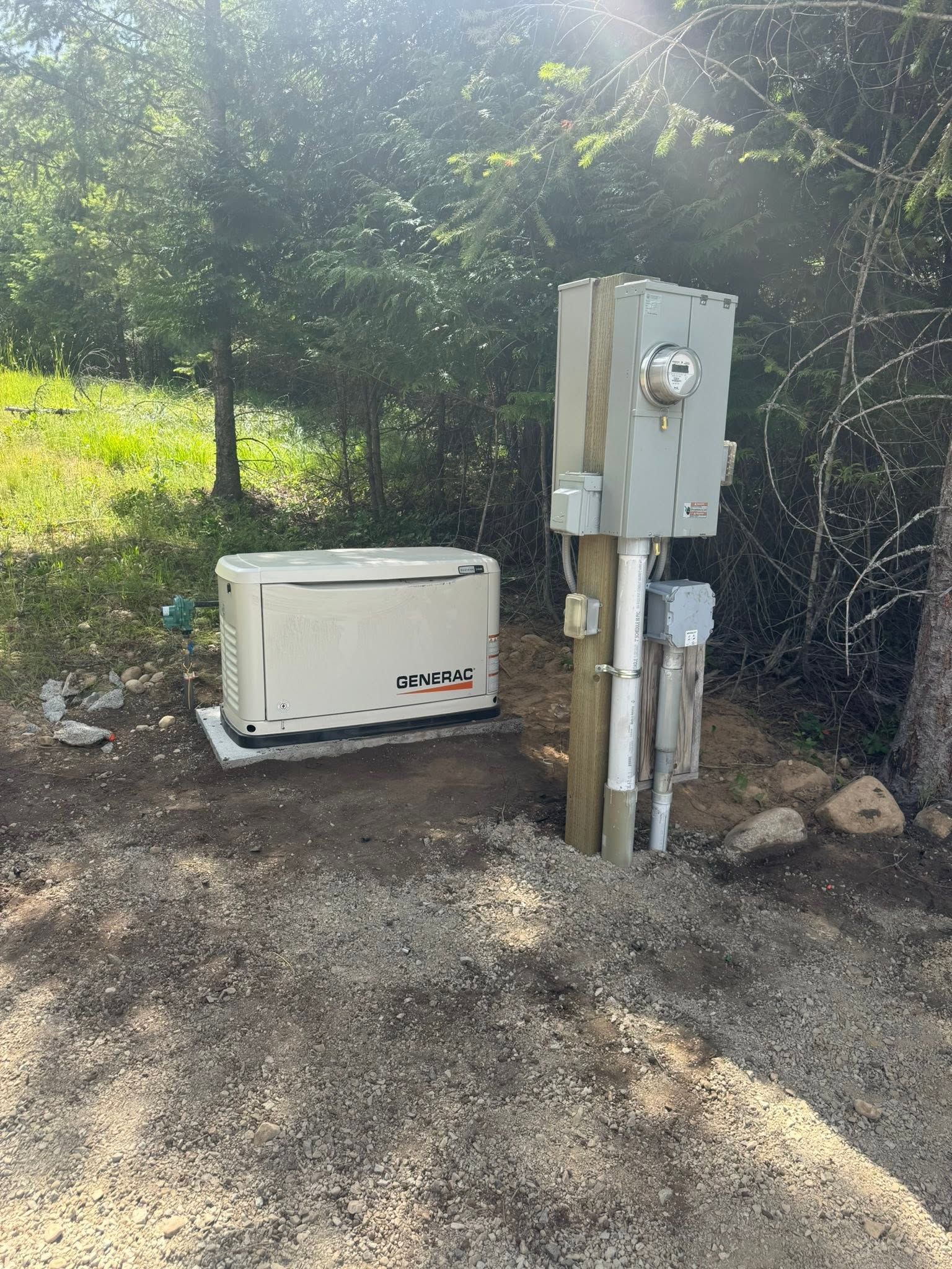 Electrical meter and utility boxes beside a white generator on a gravel driveway near trees.