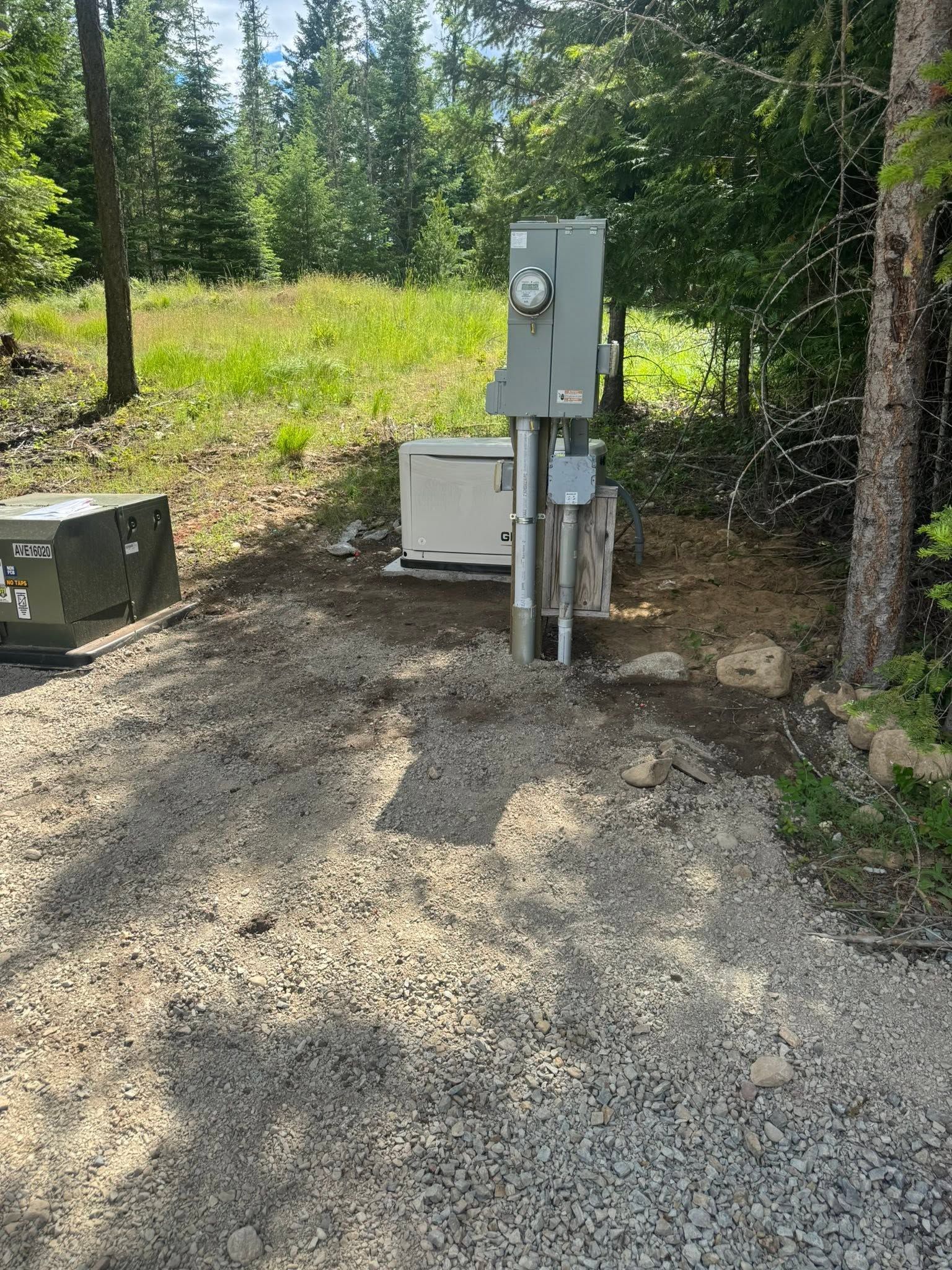 Electrical utility boxes on gravel beside trees and a grassy field