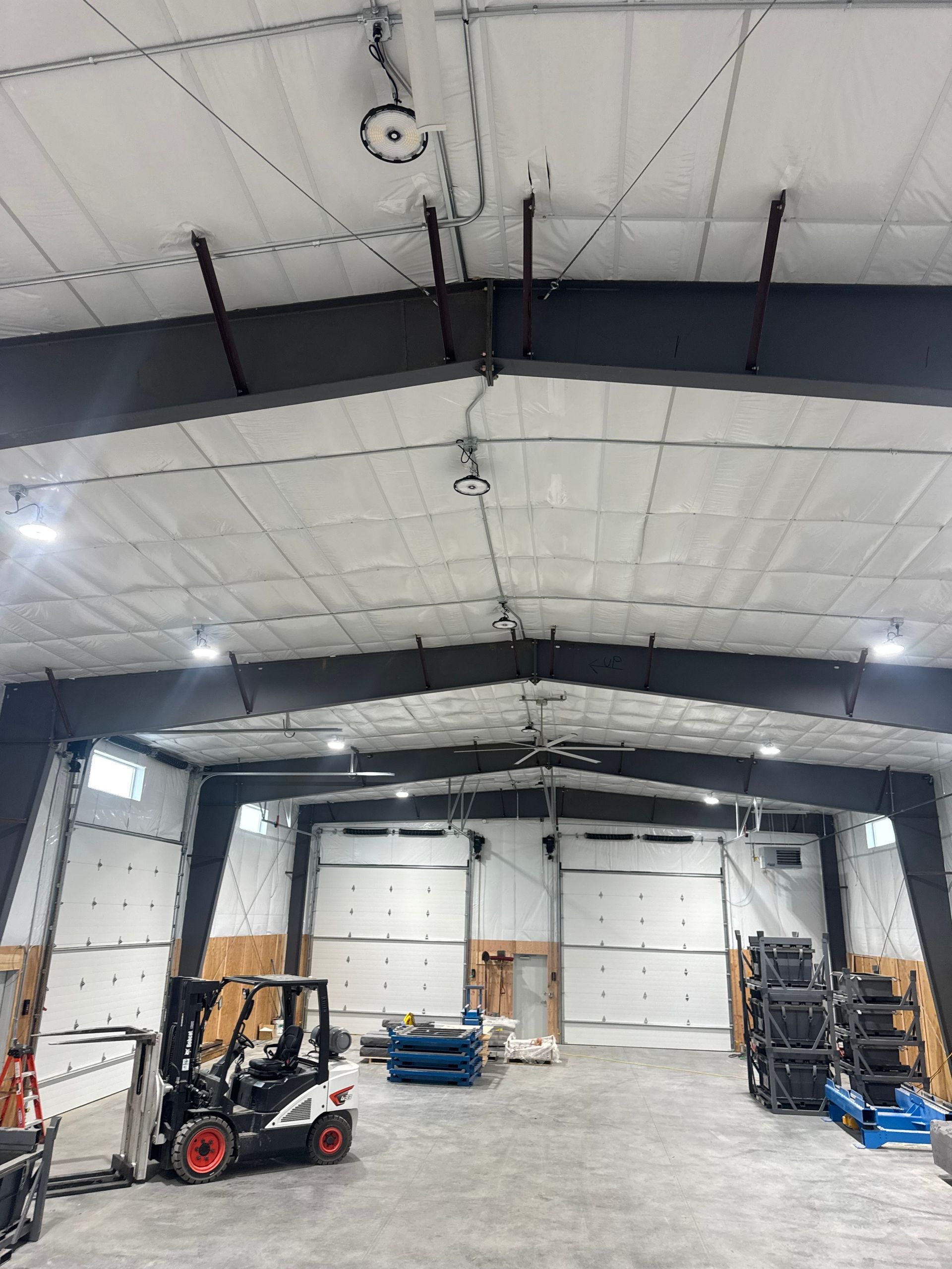 Empty industrial warehouse interior with high ceiling, forklifts, and pallets on a concrete floor
