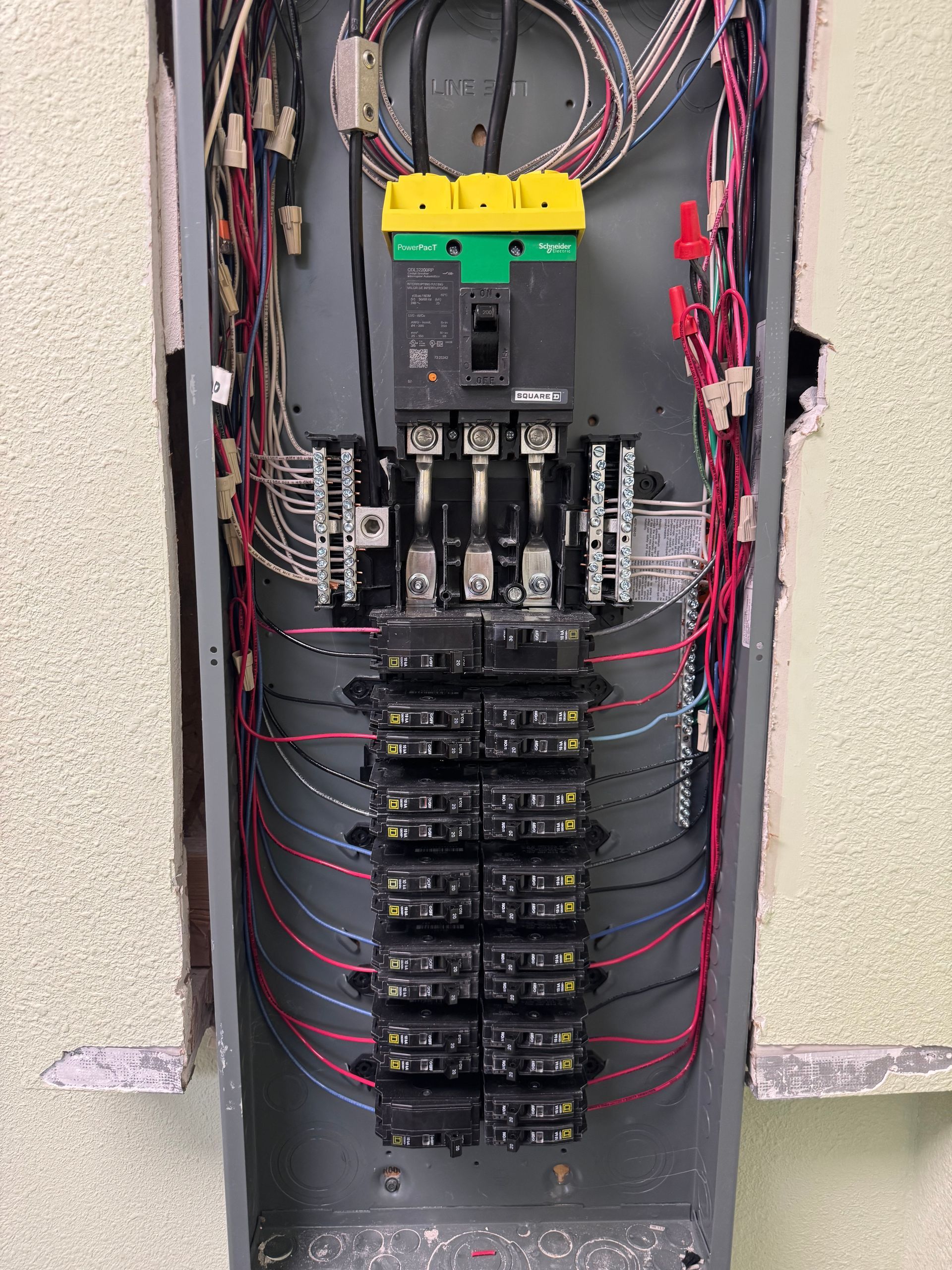Open electrical breaker panel with exposed wiring and multiple circuit breakers in a wall recess.