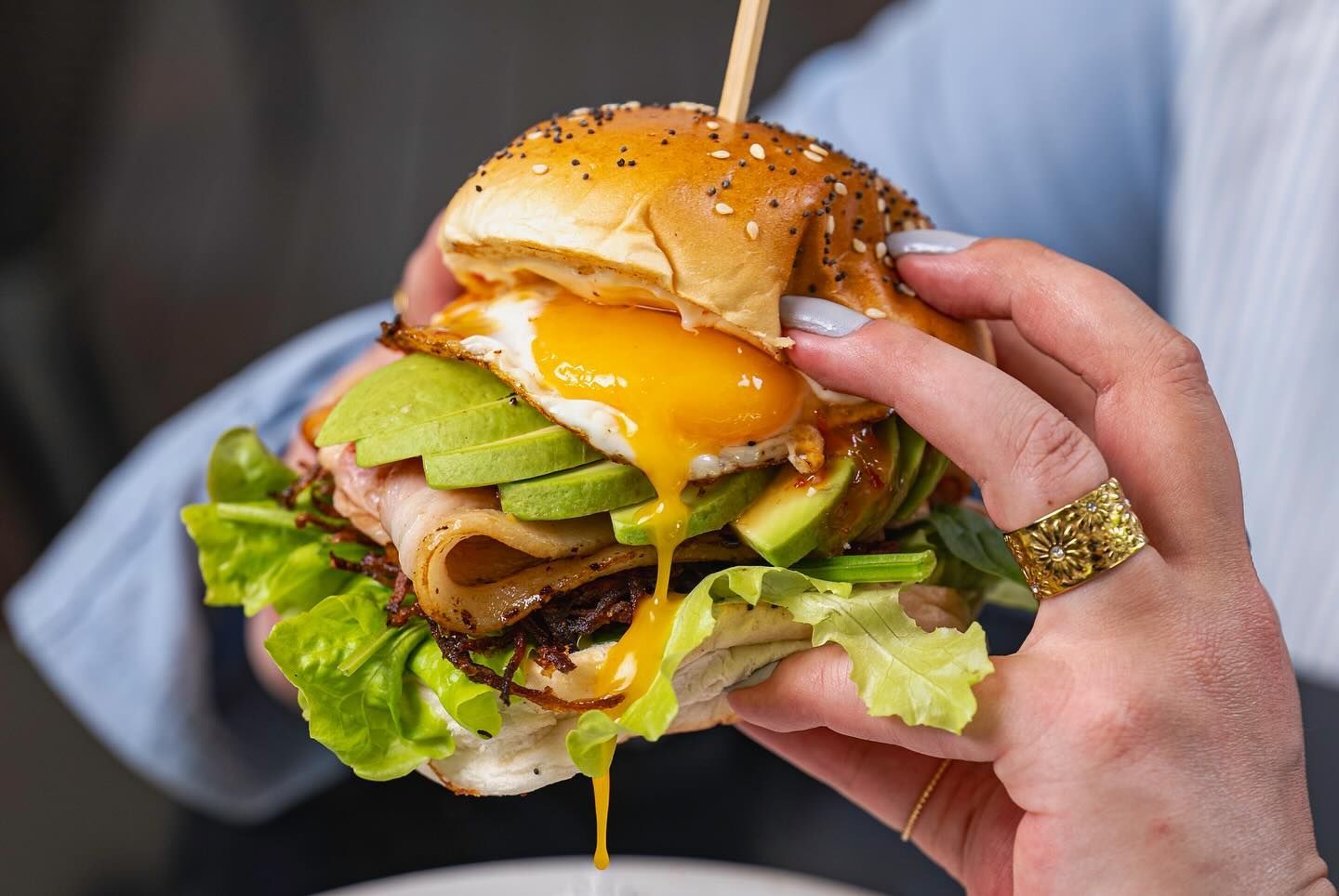 A Woman is Holding a Sandwich With Avocado, Lettuce, and Eggs on a Bun — The Pass Cafe in Byron Bay, NSW