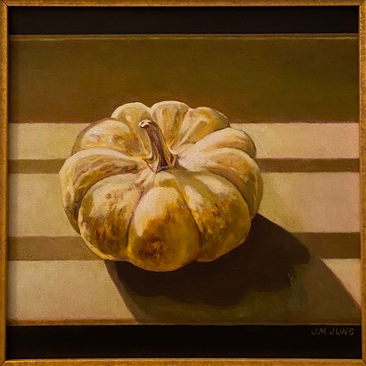 White pumpkin sitting on a windowsill with light from Venetian blinds falling over it.