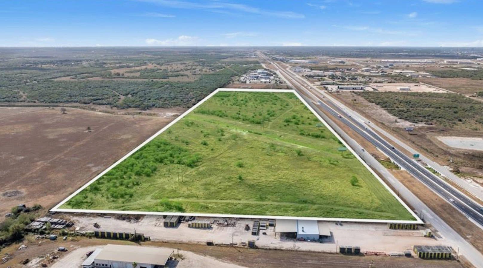 Aerial view of a large green field bordered by roads and buildings under a clear sky