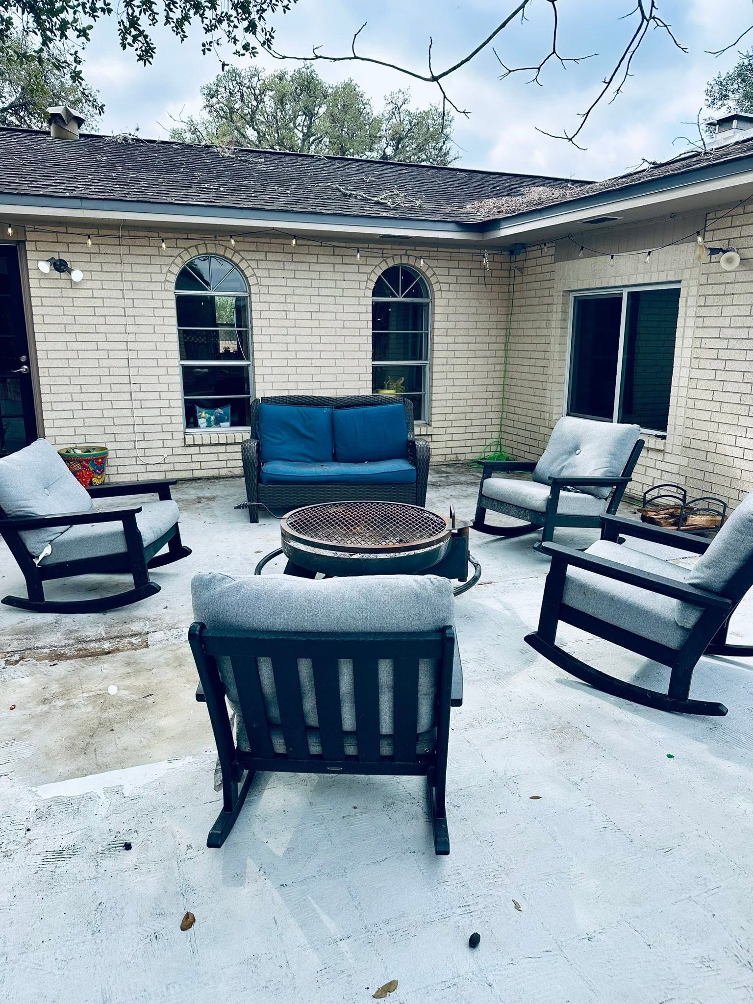 Patio with black chairs around a fire pit, blue sofa, and brick house wall with arched windows.
