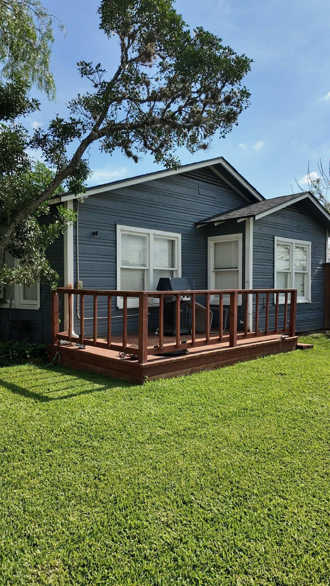 Gray house with white shutters and a red wooden porch in a sunny grassy yard