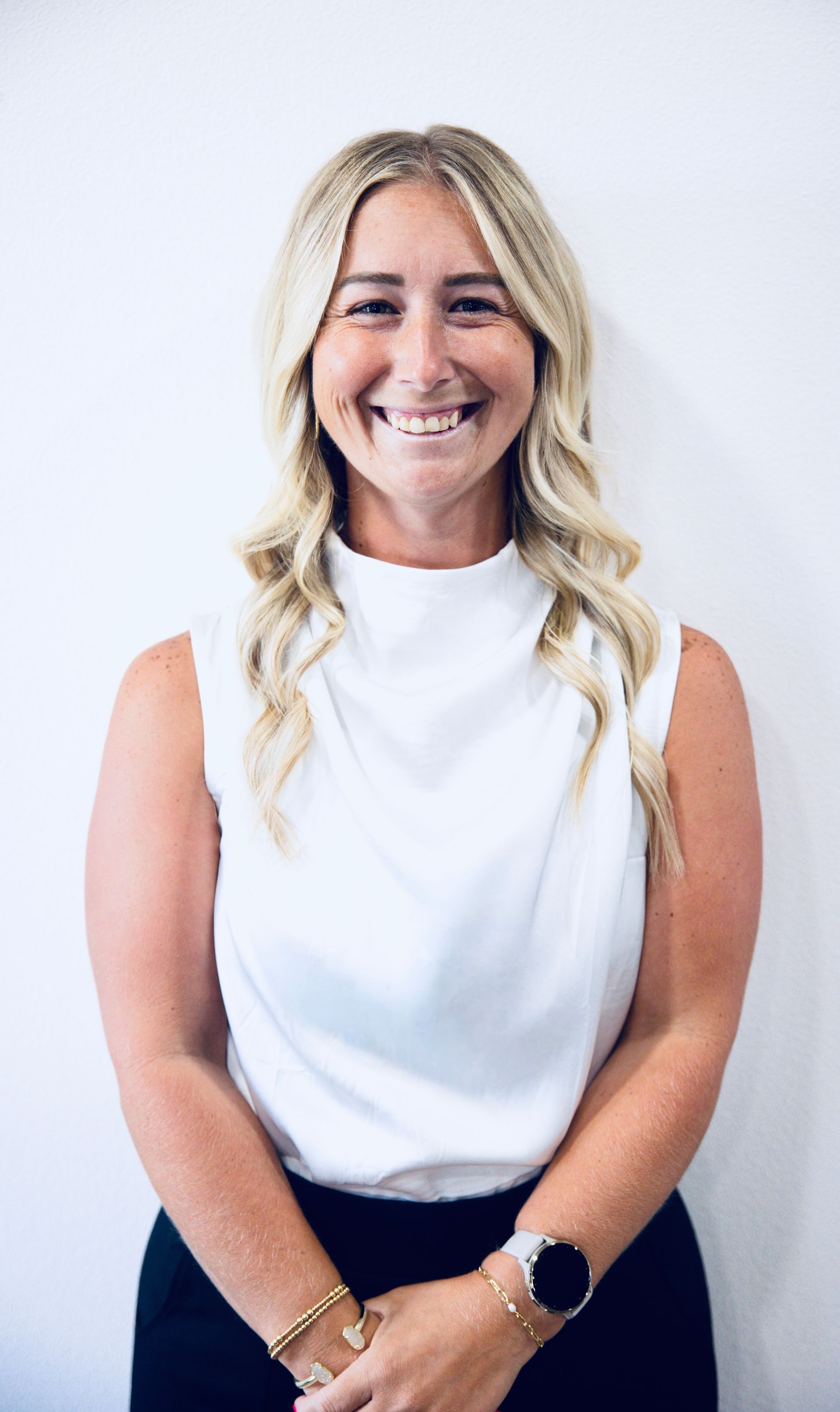 Smiling woman in a white sleeveless top against a plain light background