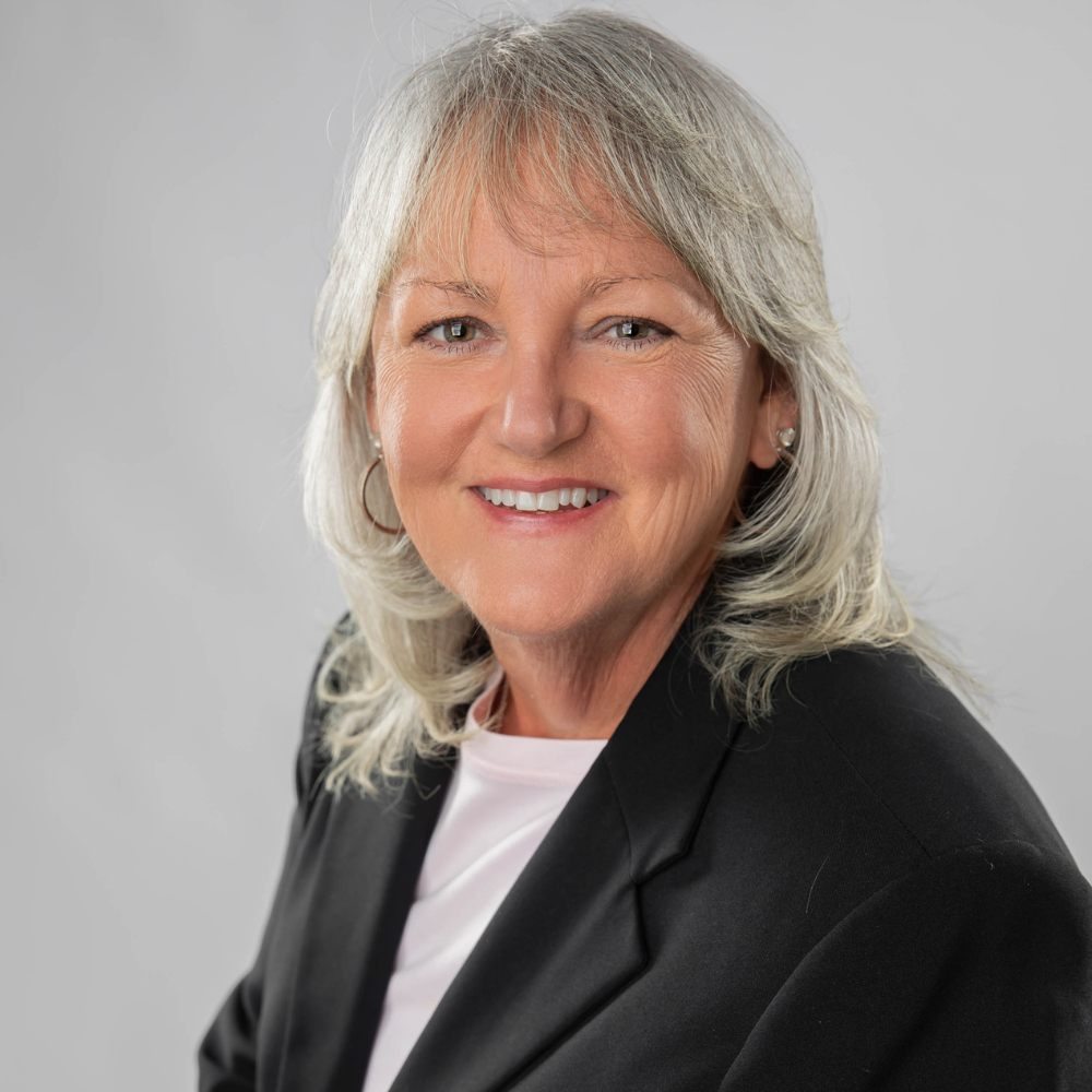Portrait of a smiling woman in a black blazer against a light gray background