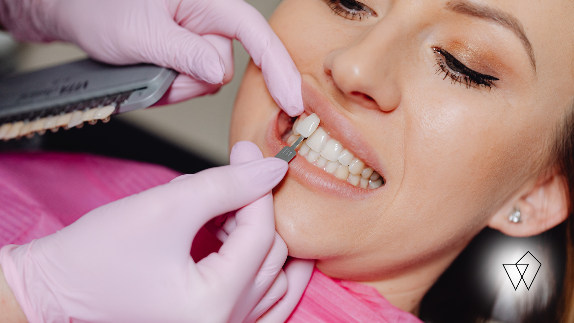 Dentist wearing pink gloves examining a patient’s teeth with a dental tool in a clinic