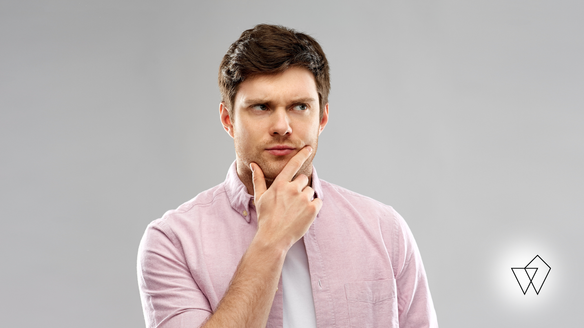 Man in a pink shirt touching his chin, looking thoughtful against a gray background