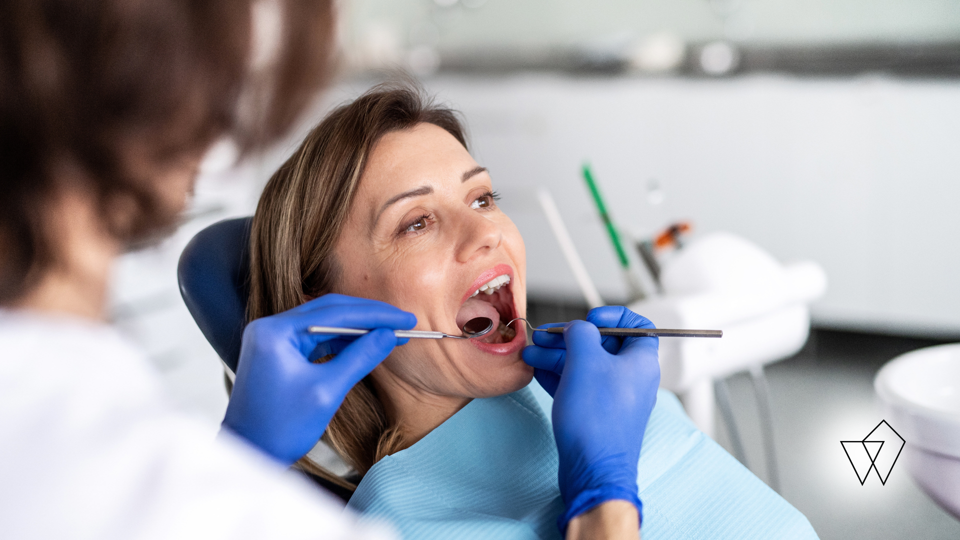 Dentist examining a woman's open mouth with gloved hands in a dental clinic