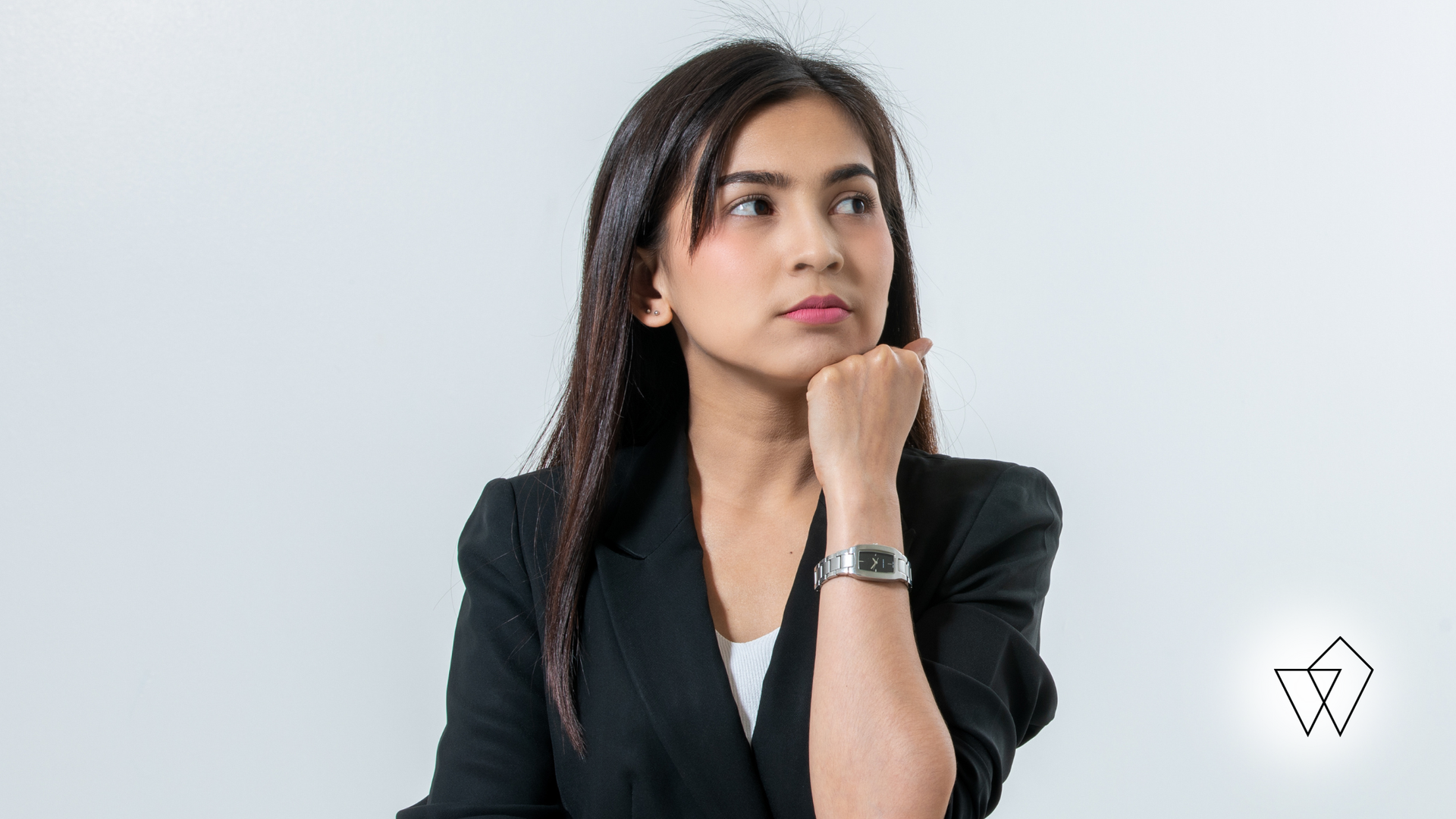 Woman in a black blazer posing thoughtfully against a light gray background.