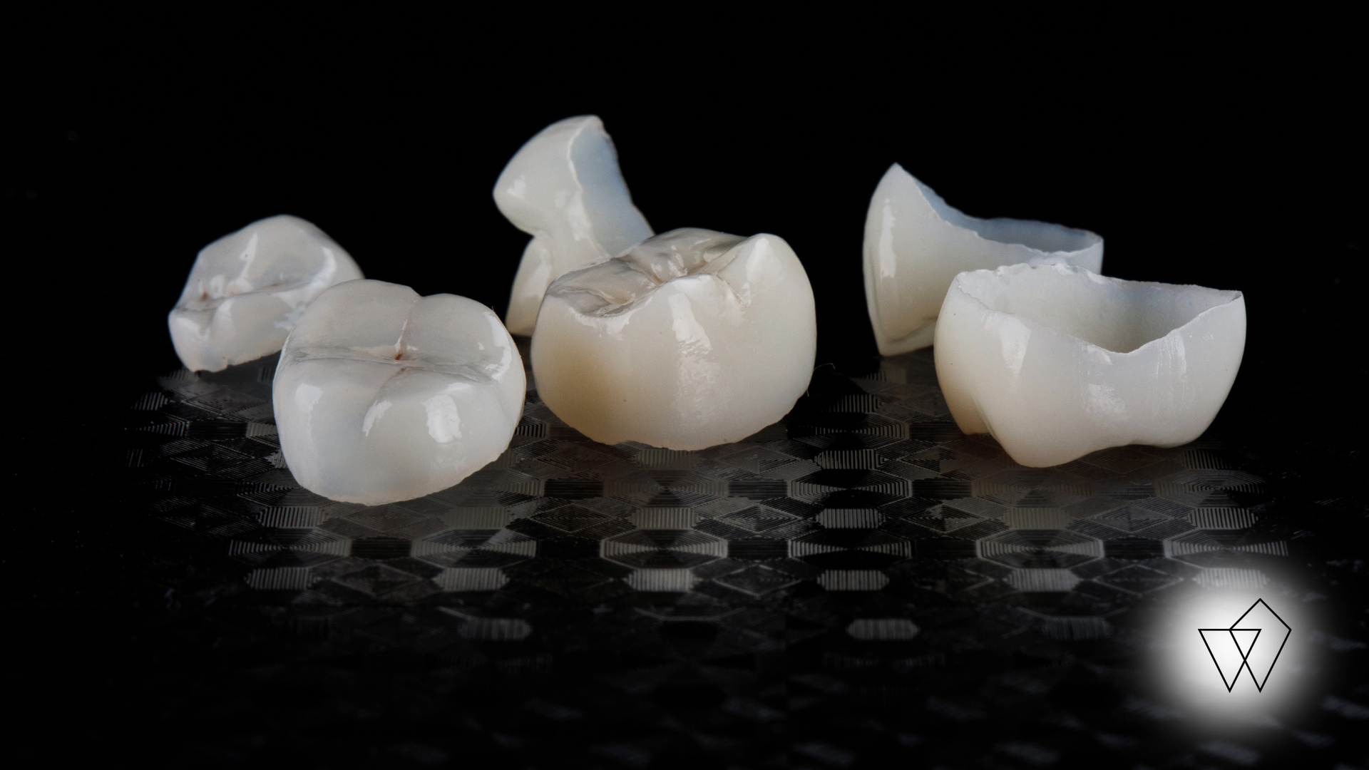 Three white dental crowns or tooth prosthetics displayed on a black surface.