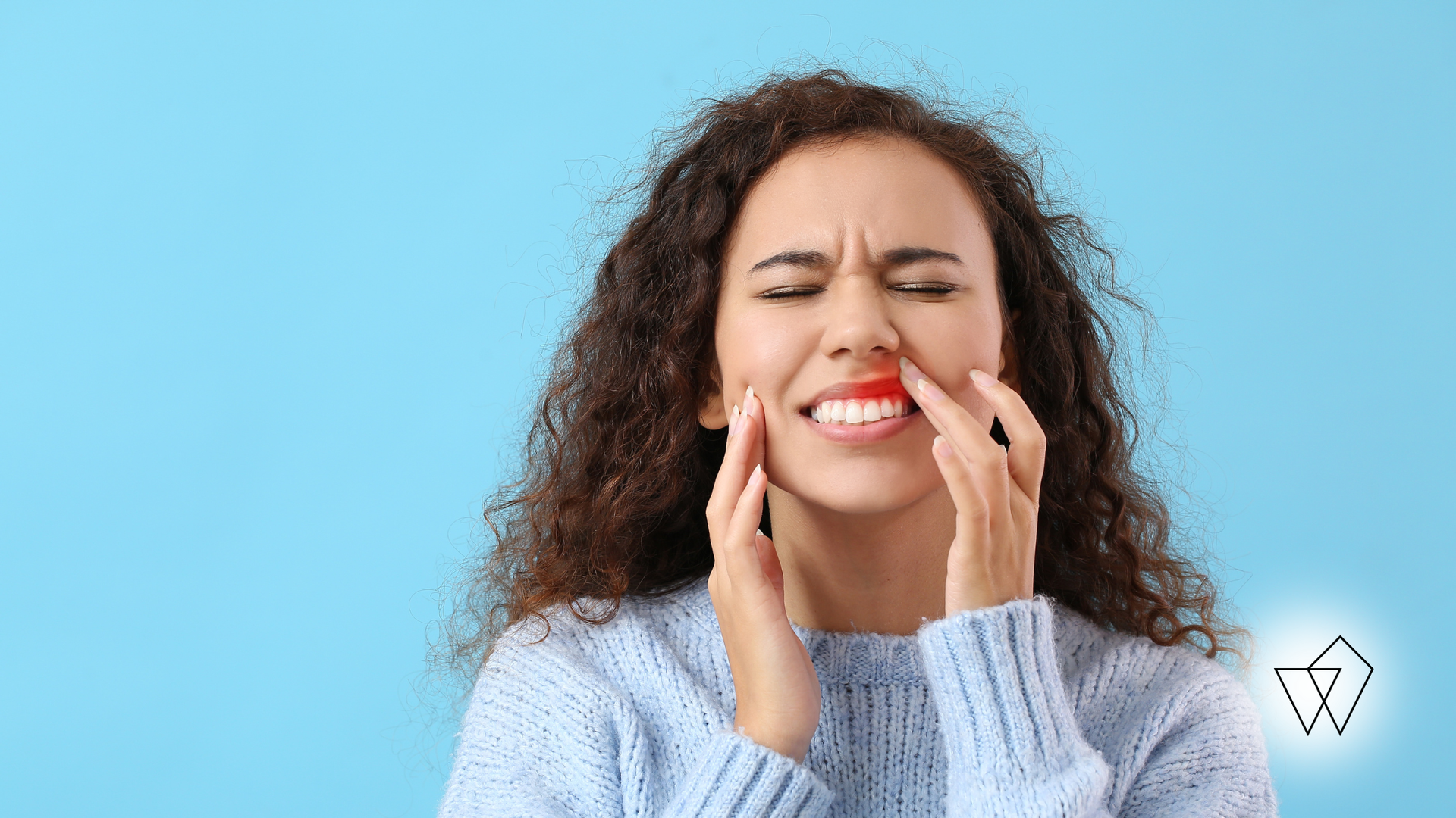 Woman grimacing and holding her cheek, suggesting tooth pain, against a blue background