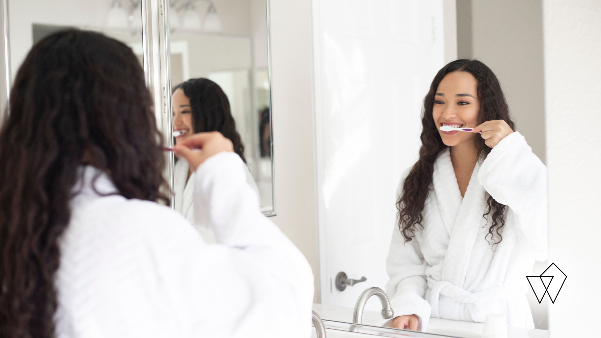 Woman brushing her teeth in a bright bathroom, seen in a mirror