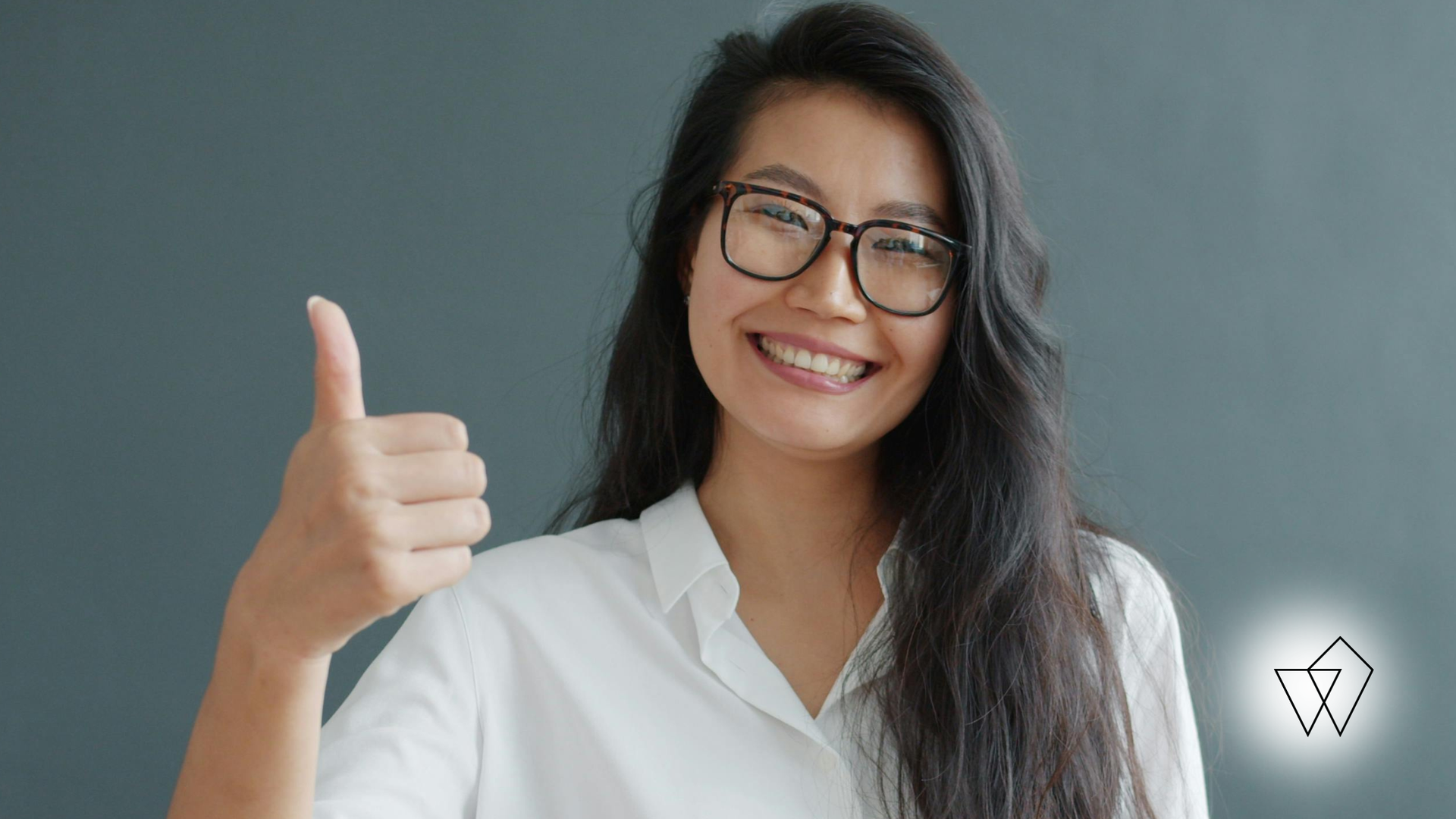 Smiling person in glasses giving a thumbs-up against a light gray background