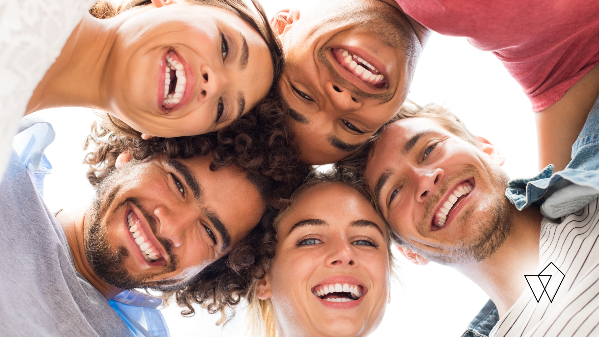 Smiling friends leaning in a circle, looking down at the camera against a bright sky.