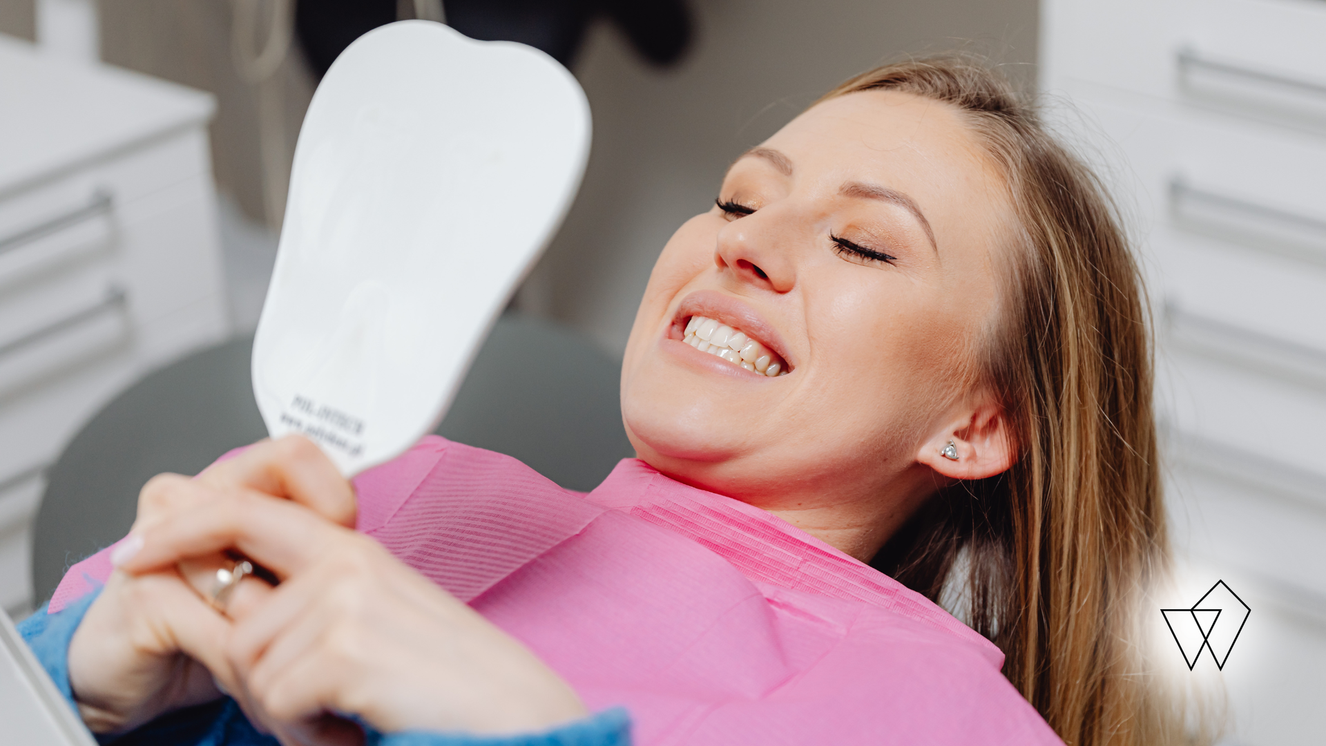 Woman reclining in a salon chair, smiling while holding a handheld mirror in a bright treatment room