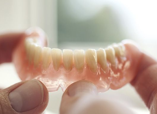 A person holding a set of upper dentures, showing pink base and white teeth.