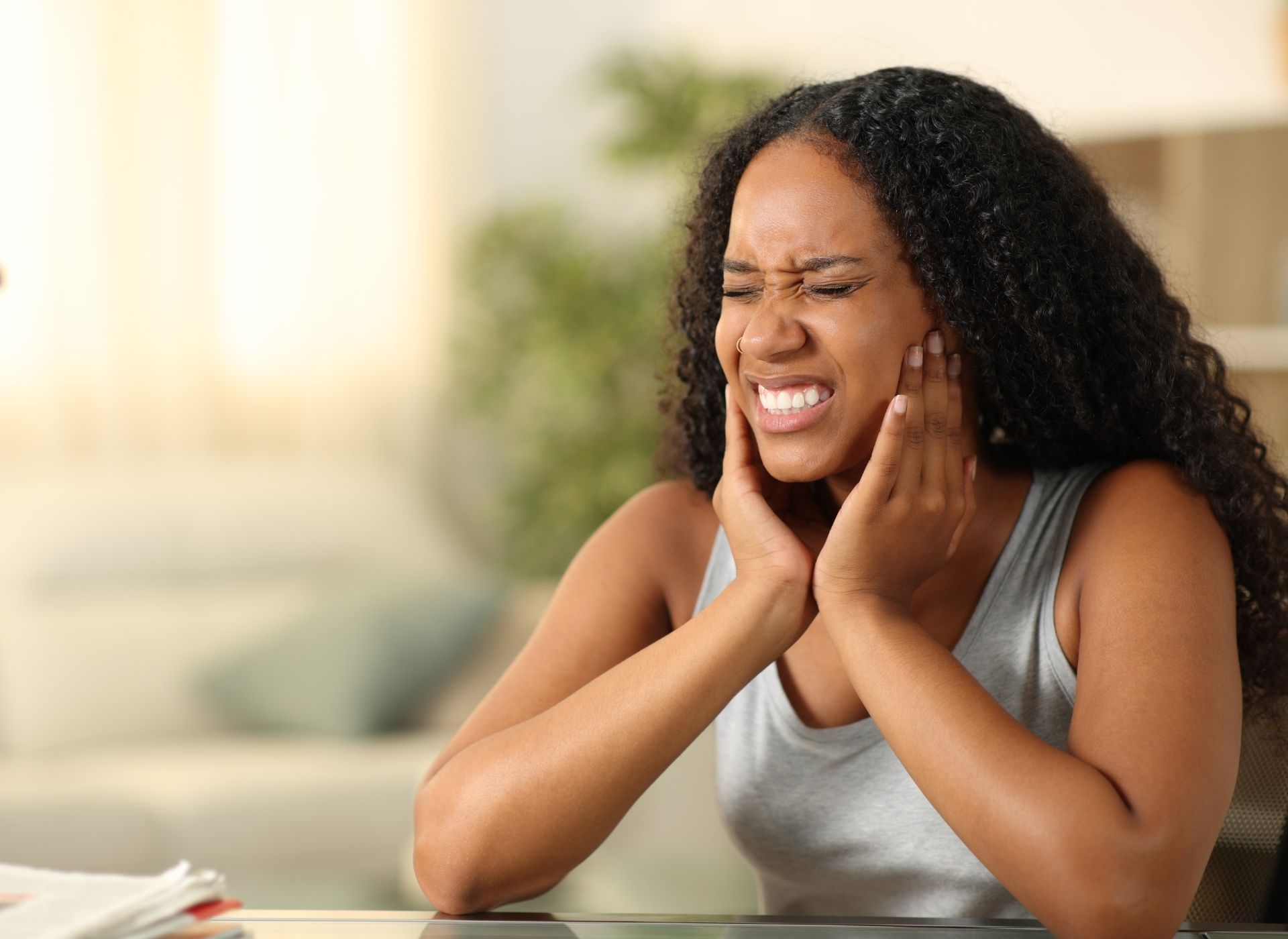 Woman experiencing severe jaw pain, holding both hands to her face, grimacing.